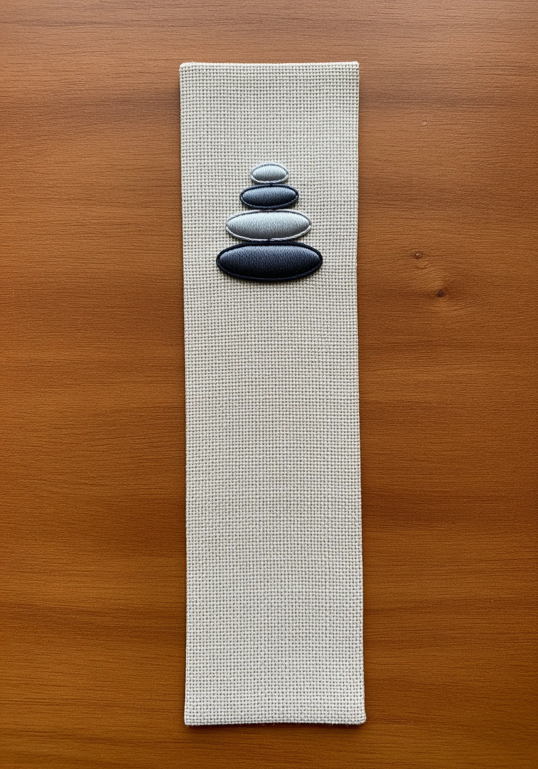 Stacked zen stones with smooth grey-to-black gradients embroidered on a fabric bookmark.