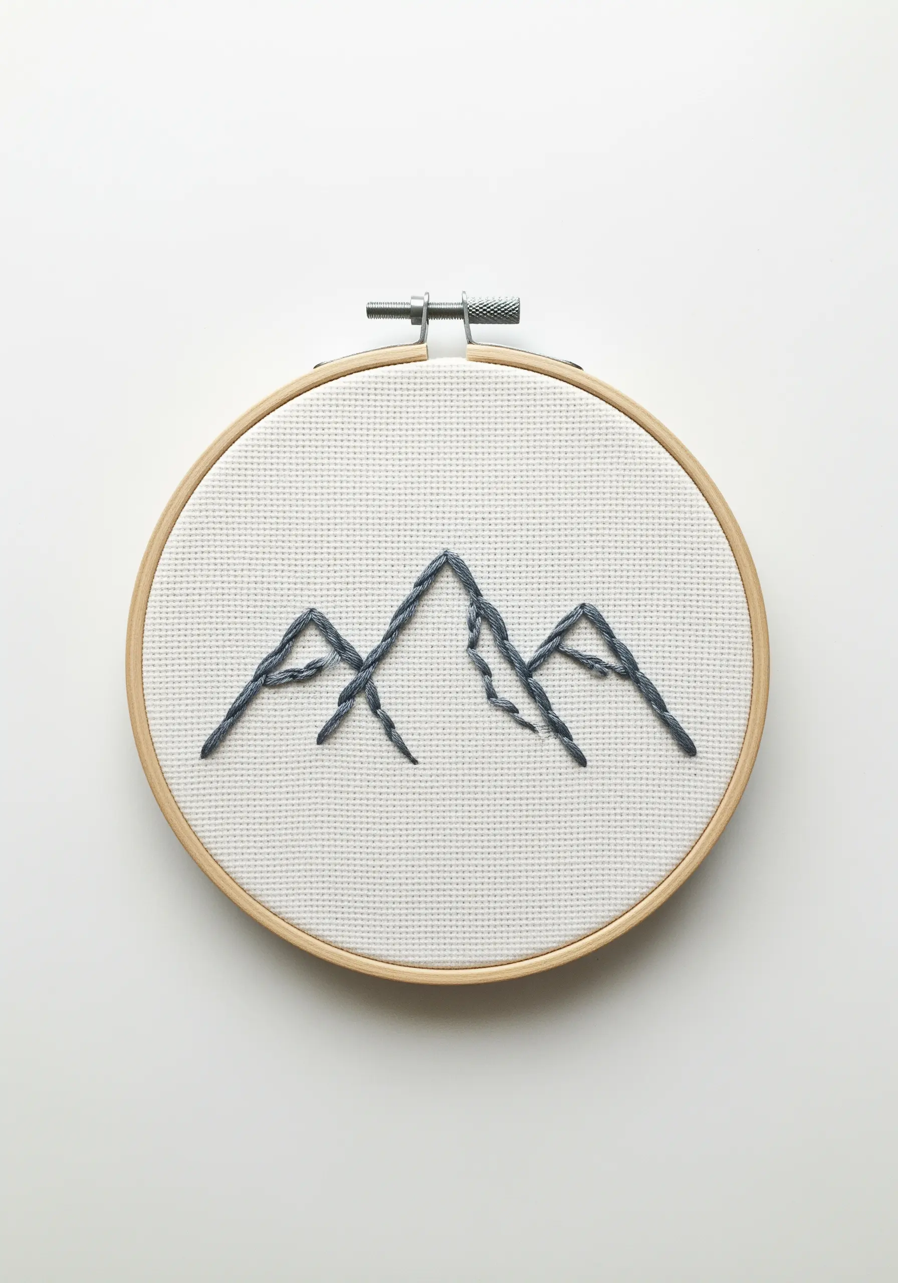 A minimalist embroidery of three mountain peaks using gray, varied straight stitches.