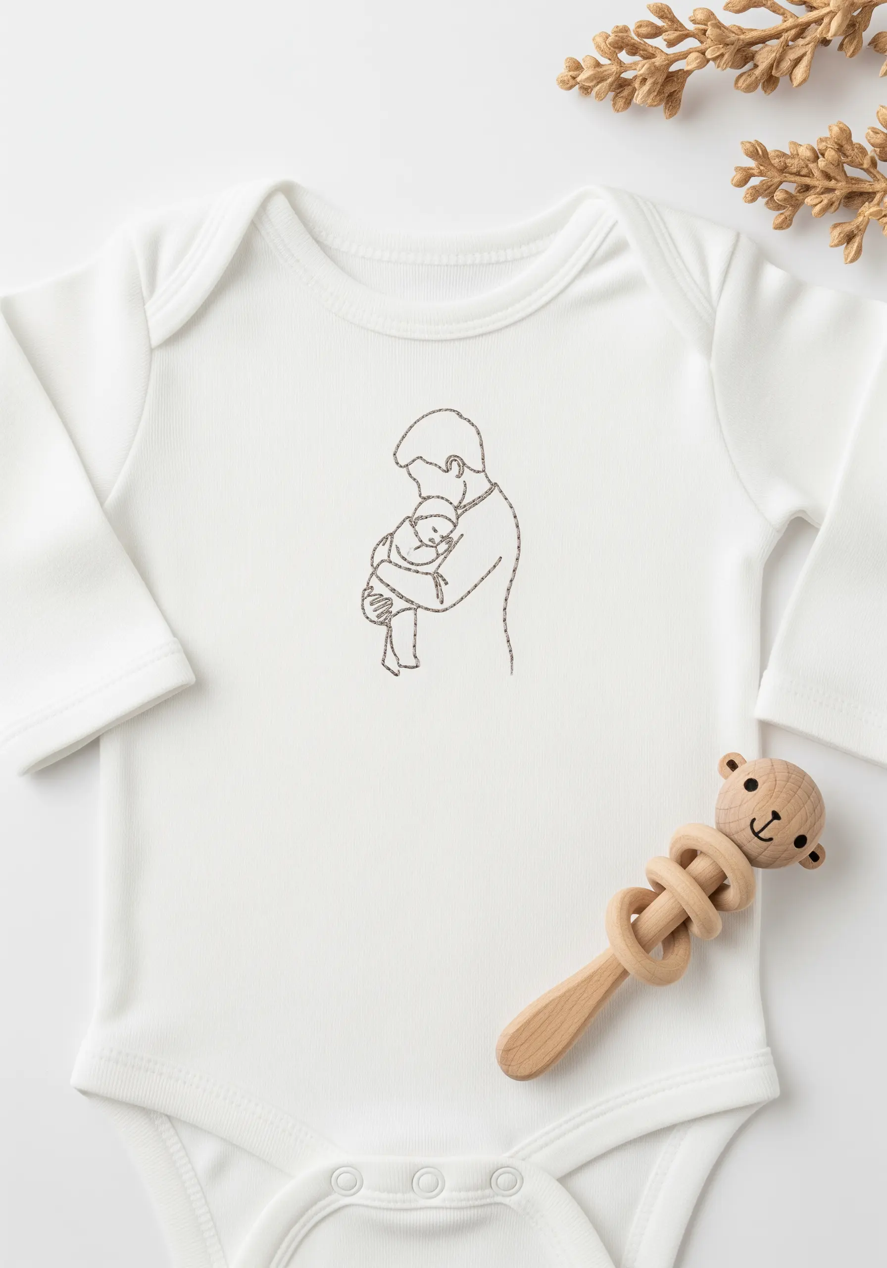 A simple outline of a father holding a baby, stitched onto the front of a white baby onesie.