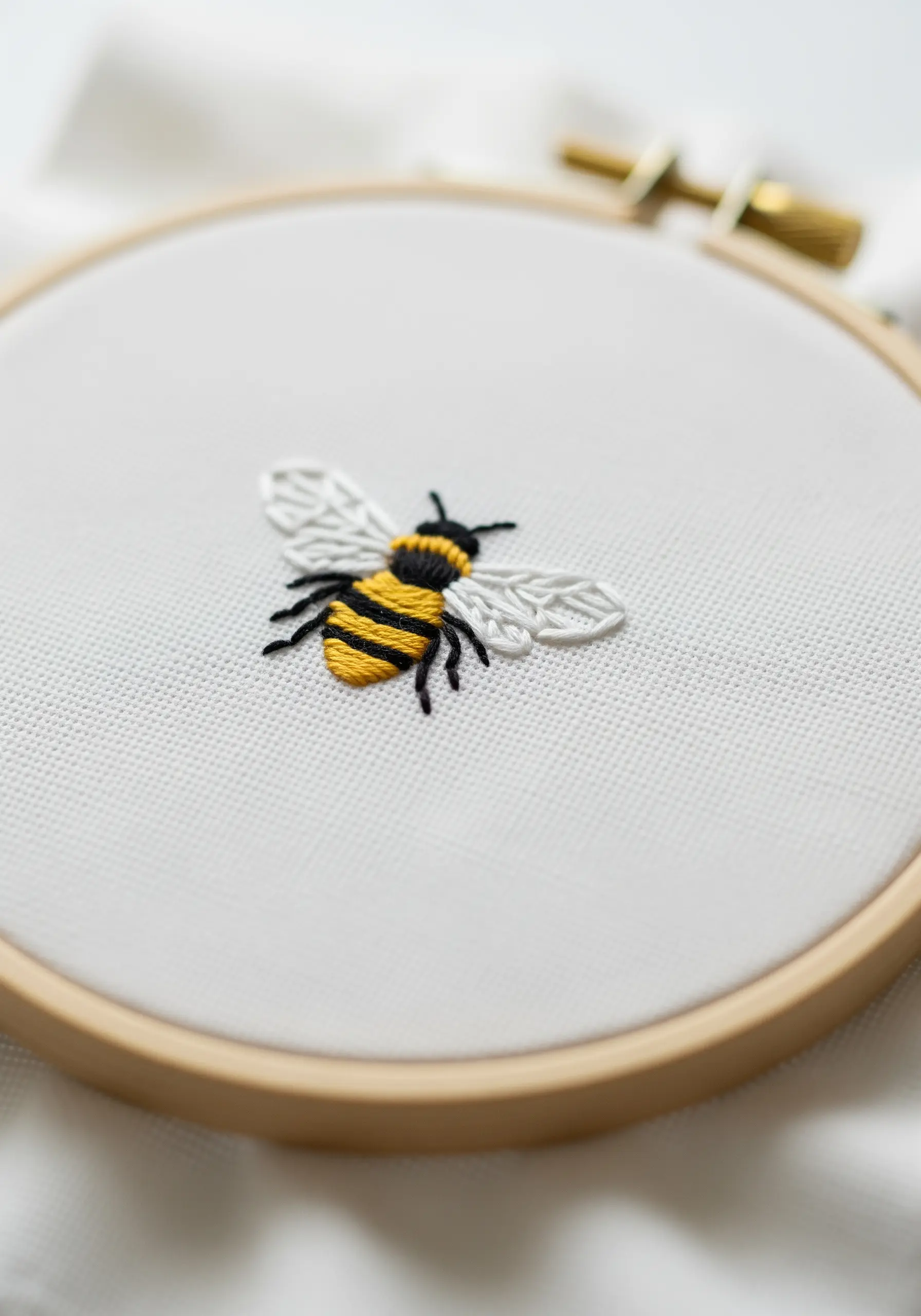 A small, detailed embroidery of a bumblebee with yellow and black satin stitch stripes.