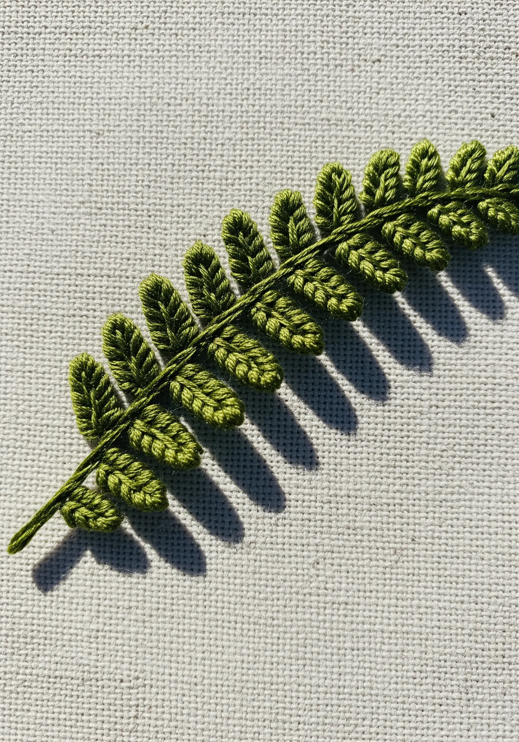A single green embroidered fern leaf with a solid gray satin-stitched shadow.