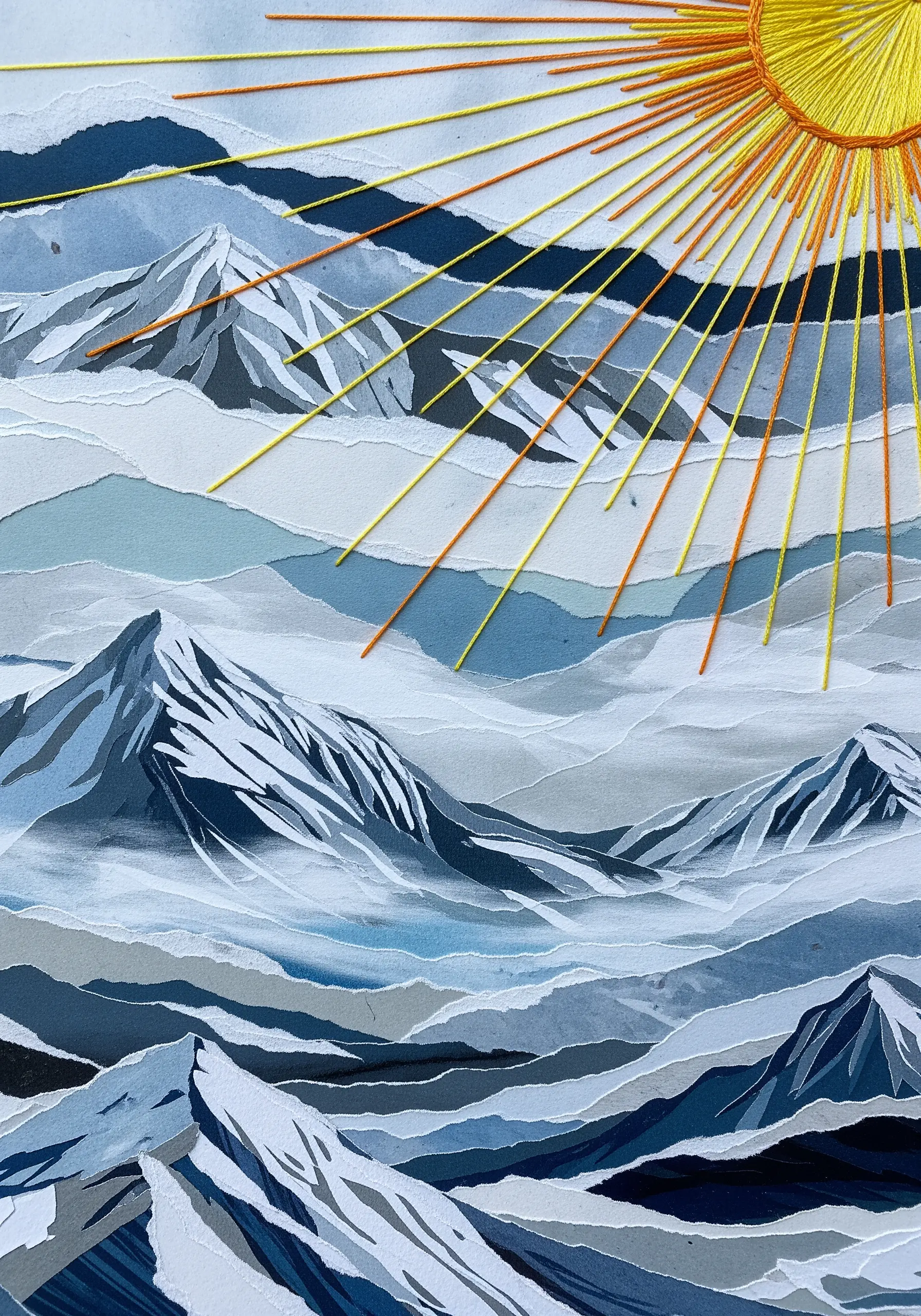 A mountain landscape collage made of torn paper with a large, bright yellow embroidered sun.