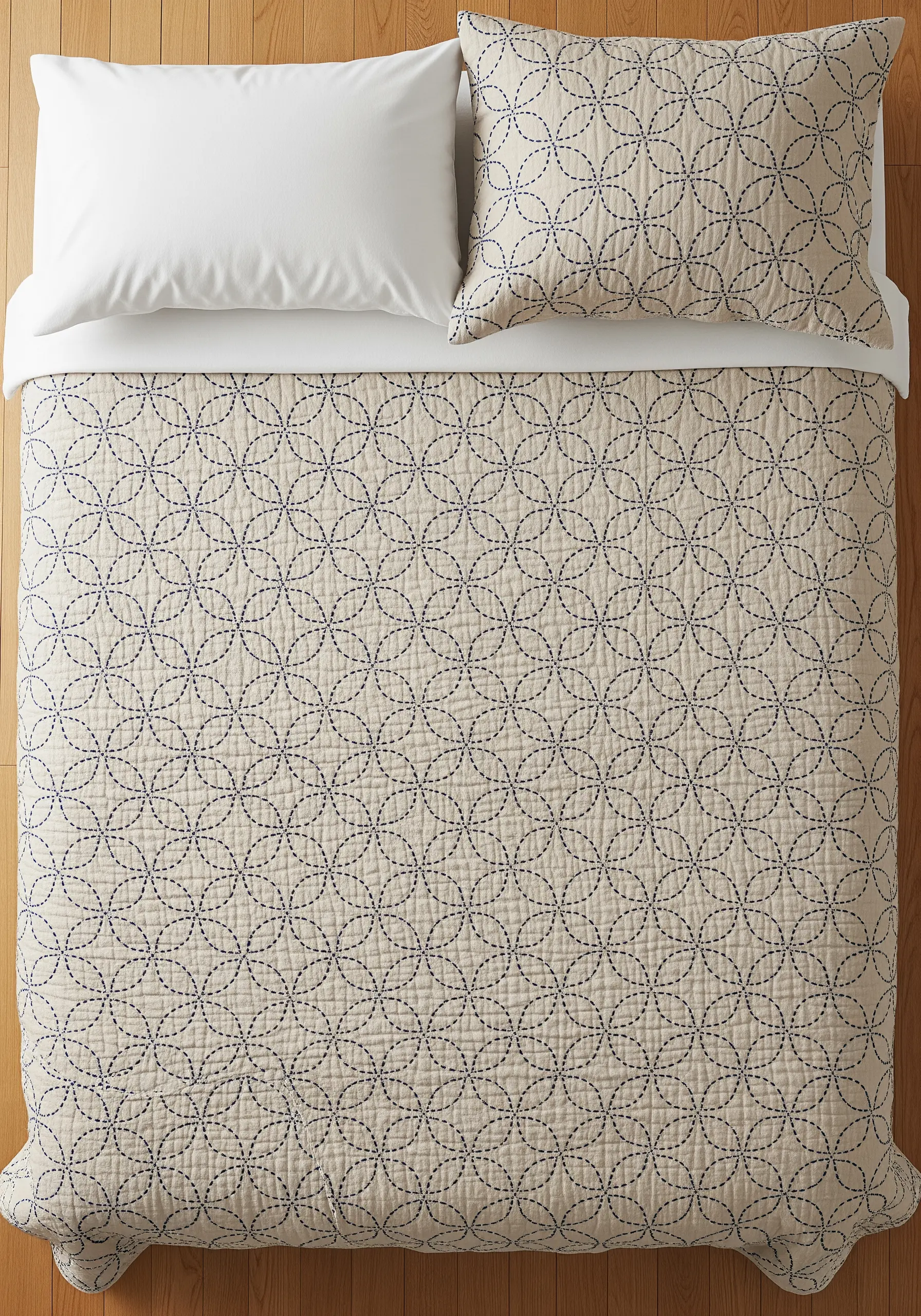 An overhead view of a bed with a beige quilt stitched with an all-over geometric circle pattern in navy blue thread.