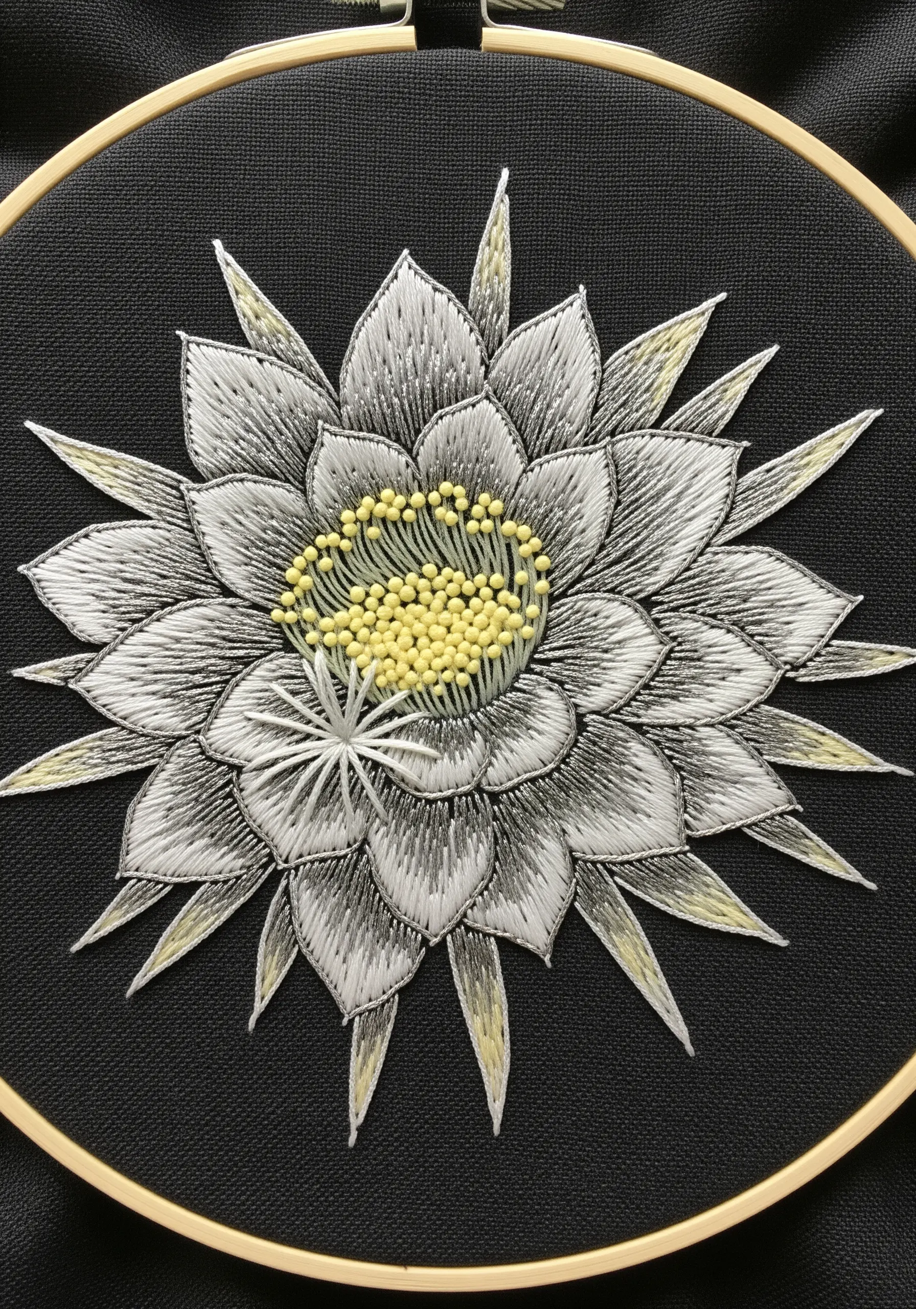 A white and grey night-blooming cereus flower embroidered on black fabric, with a yellow center.
