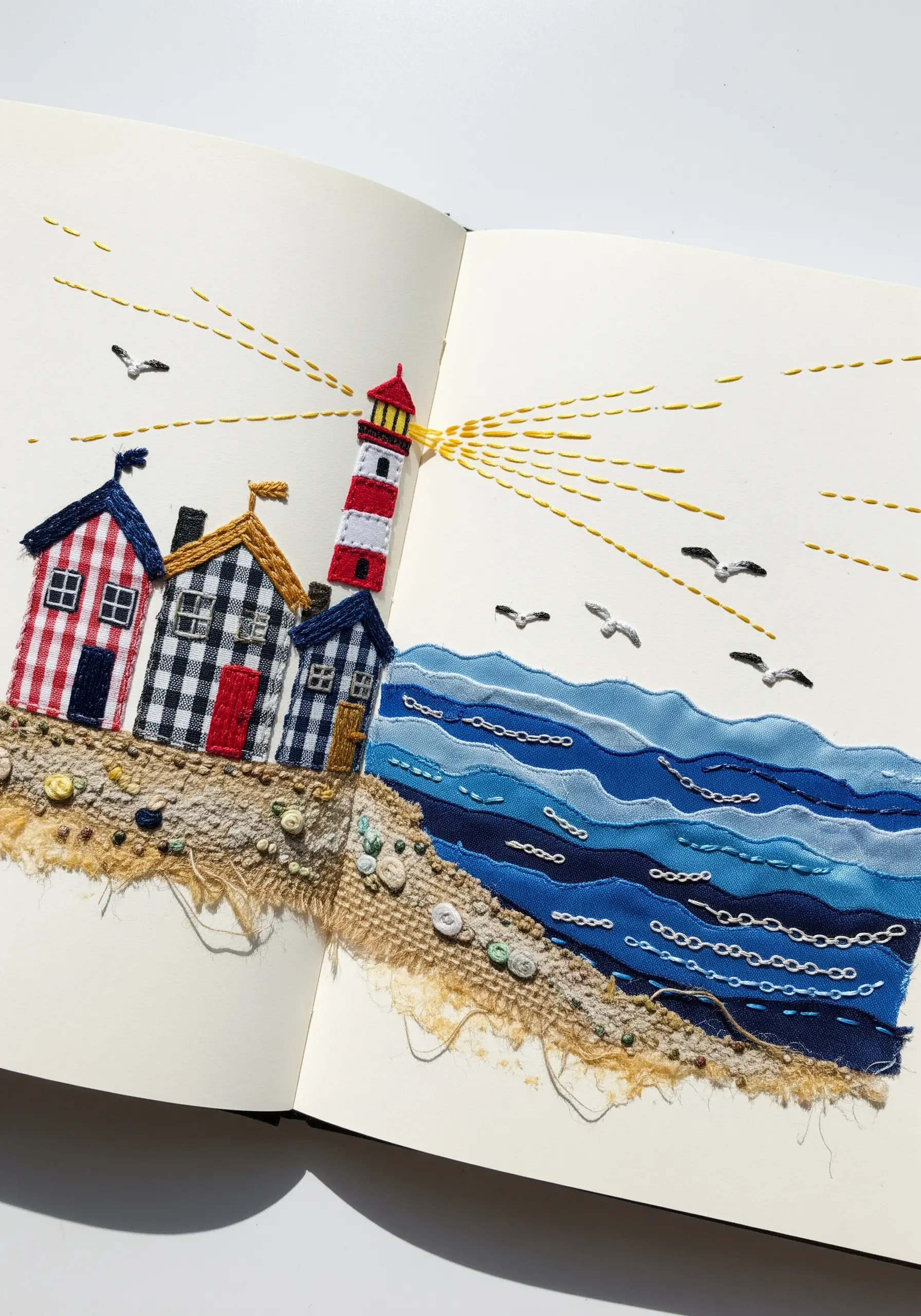 Fabric collage of a coastal scene with a lighthouse stitched into a sketchbook.