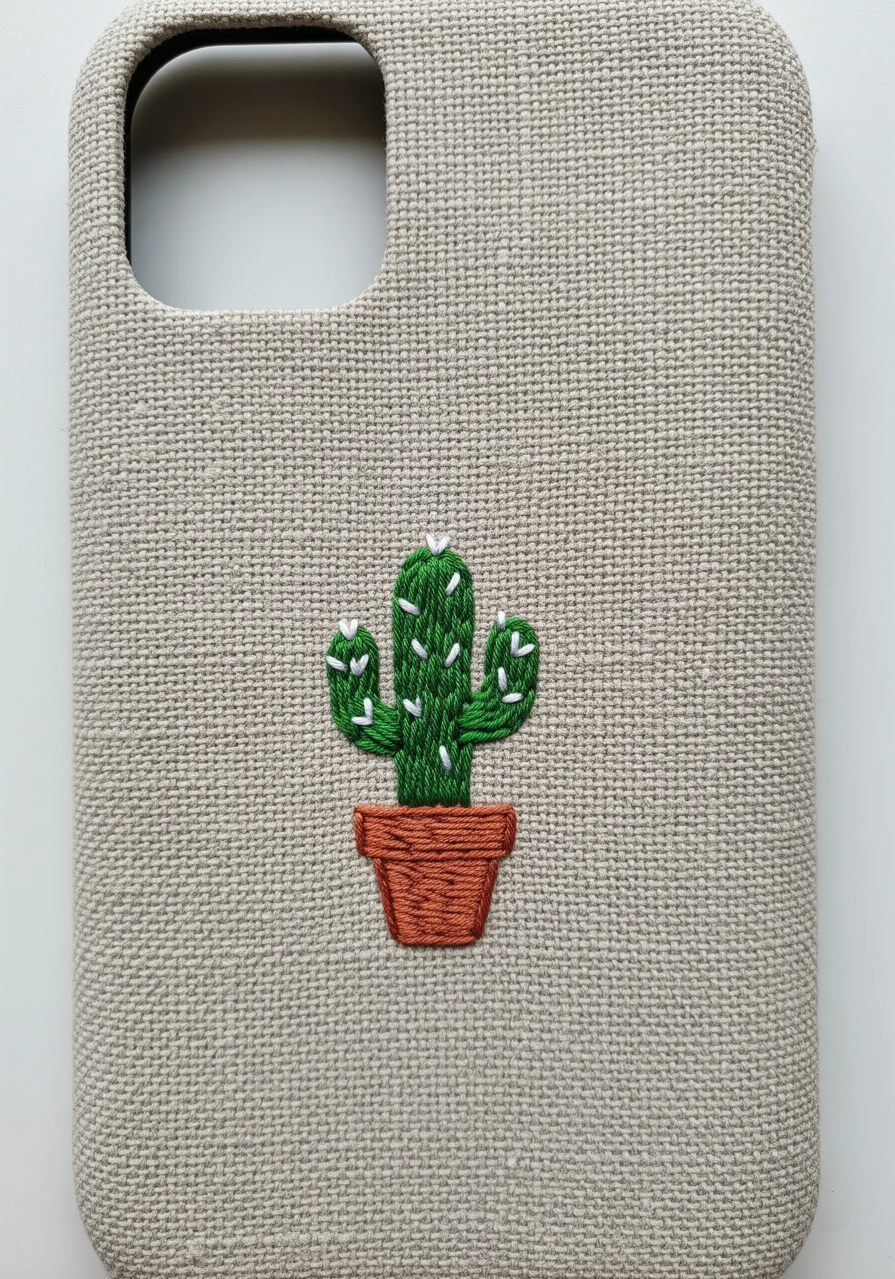 A small green cactus with white spines in a terracotta pot embroidered on a phone case.