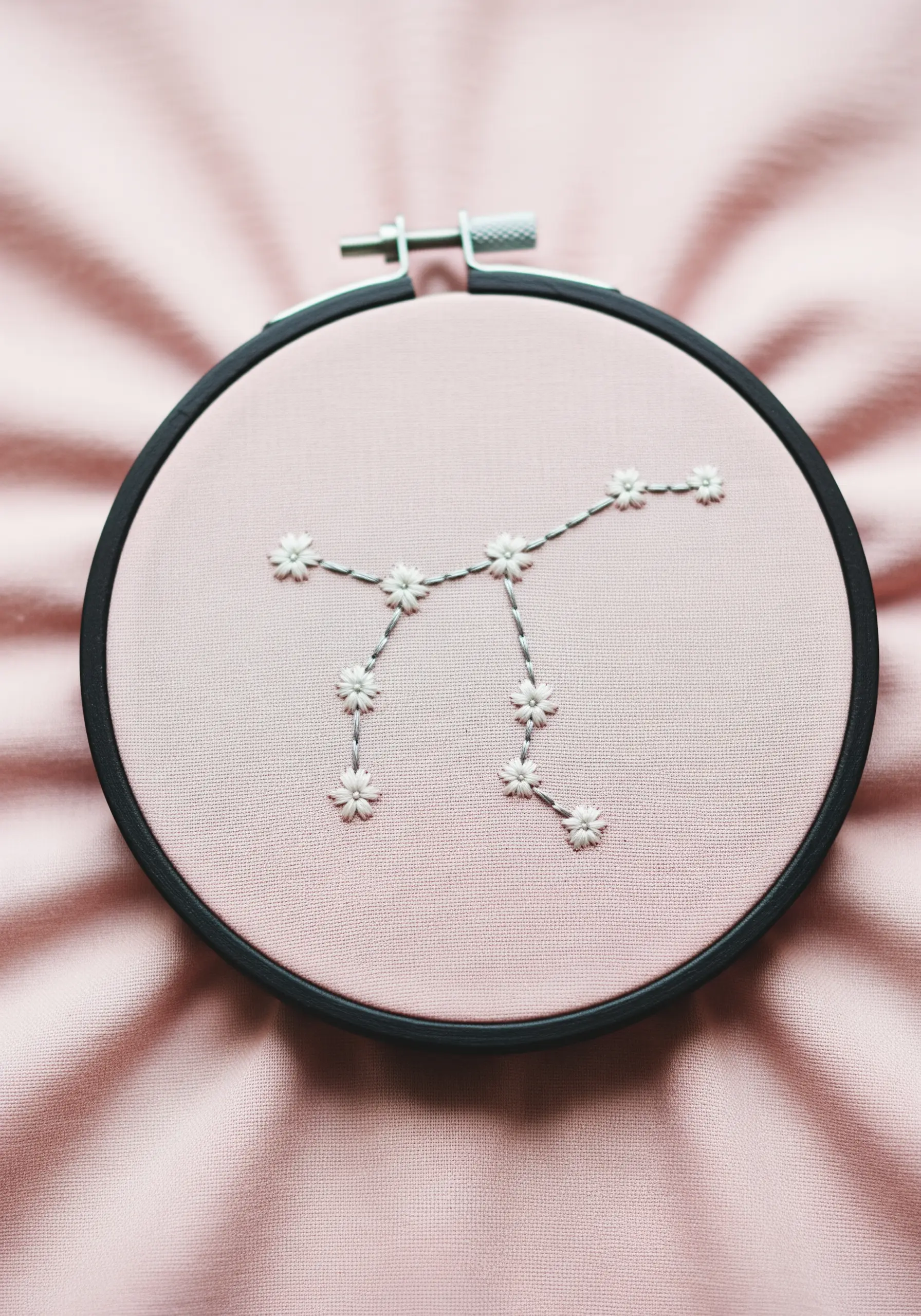 A floral constellation embroidered with white lazy daisy stitches on pink fabric.