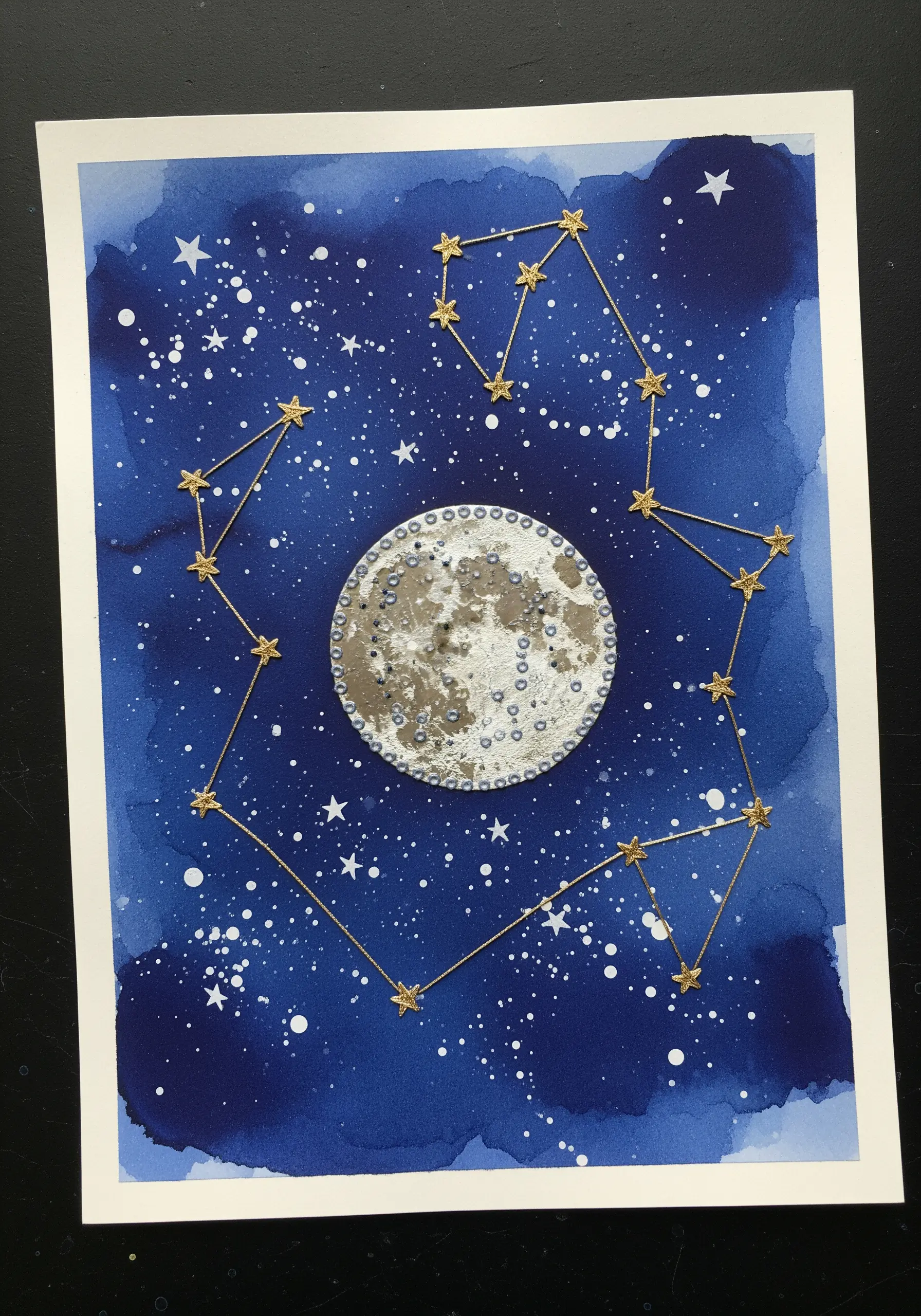 A stitched constellation in gold metallic thread over a watercolor night sky with a textured moon.