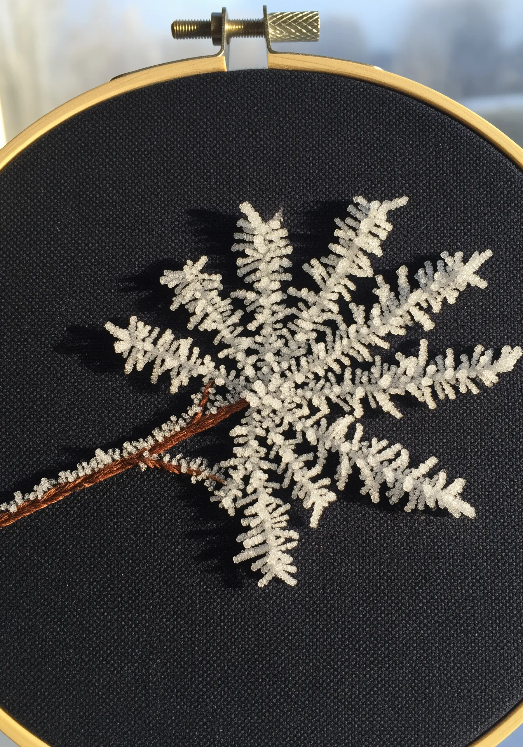 Embroidery of a delicate white hoarfrost crystal on dark navy fabric.