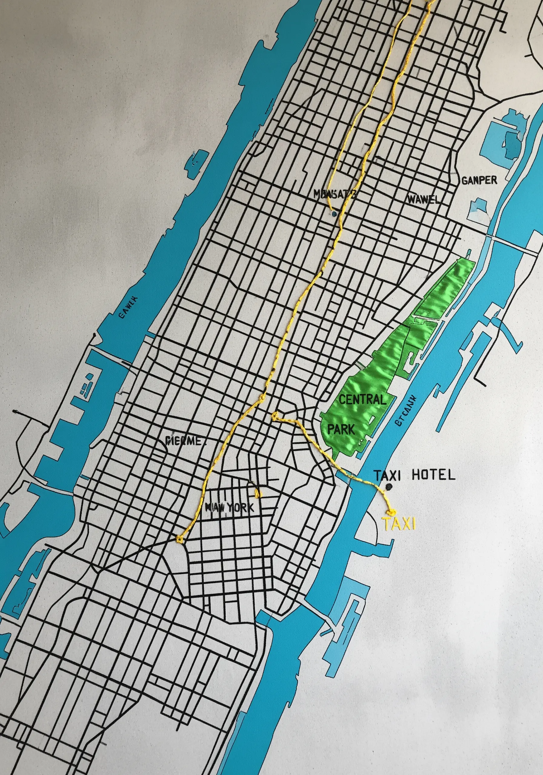 A printed map of New York City with a yellow running stitch tracing a route through Manhattan.