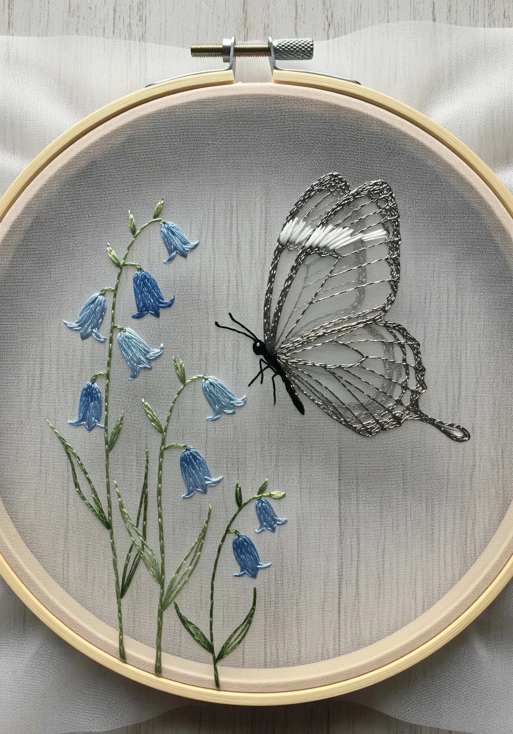 A translucent 'glasswing' butterfly embroidered on sheer fabric with delicate bluebells.