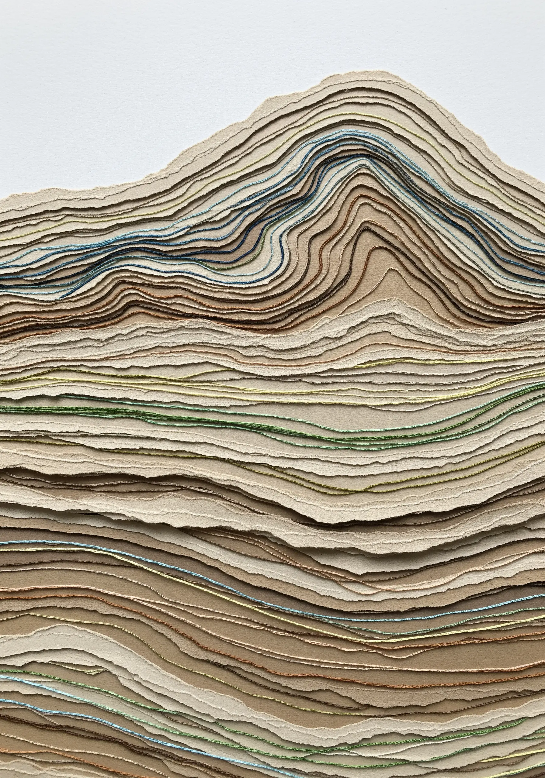 A topographical sculpture made of stacked, torn paper with subtle threads stitched through layers.