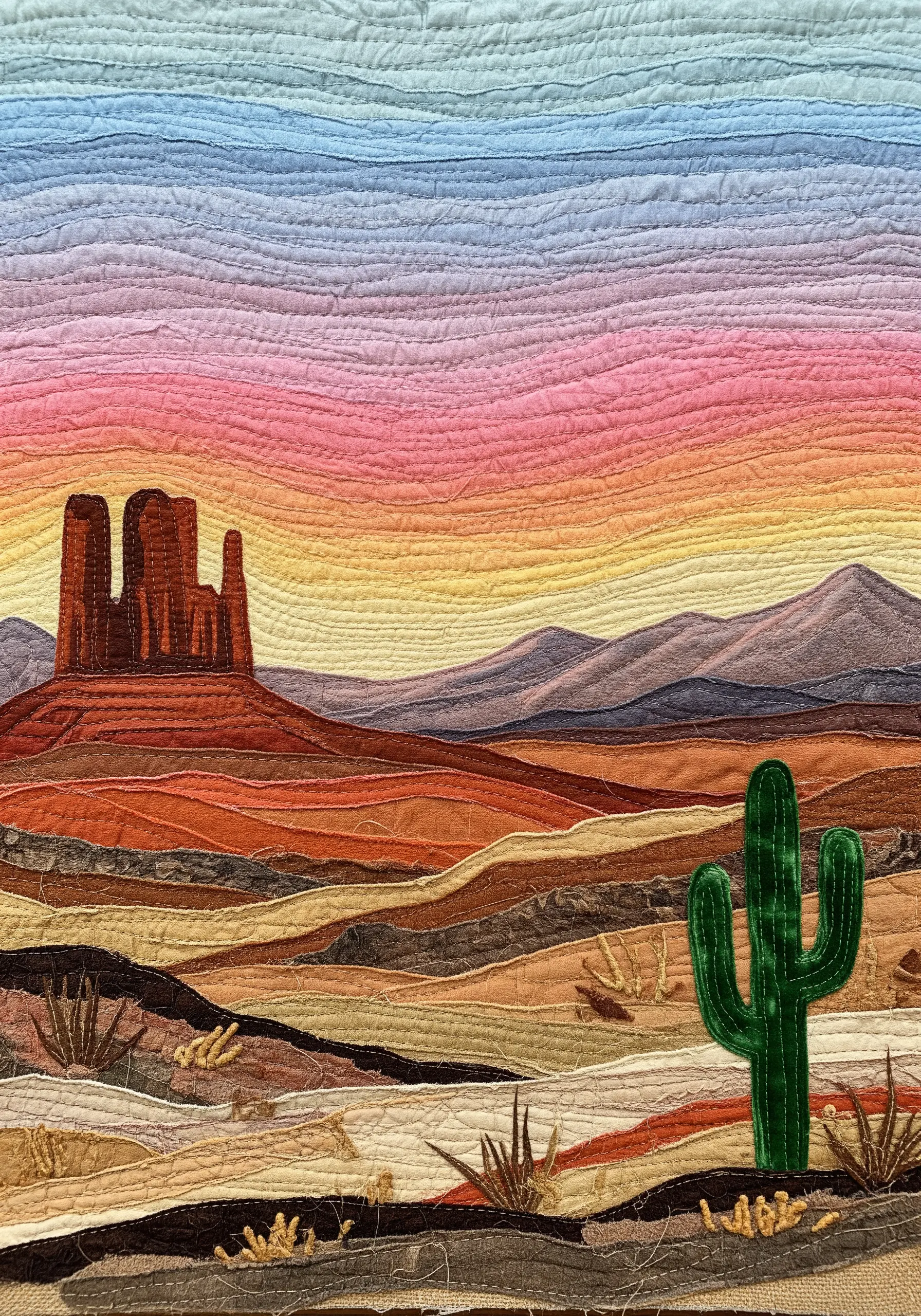 Quilted fabric collage landscape of a desert scene with layered textures and colors.