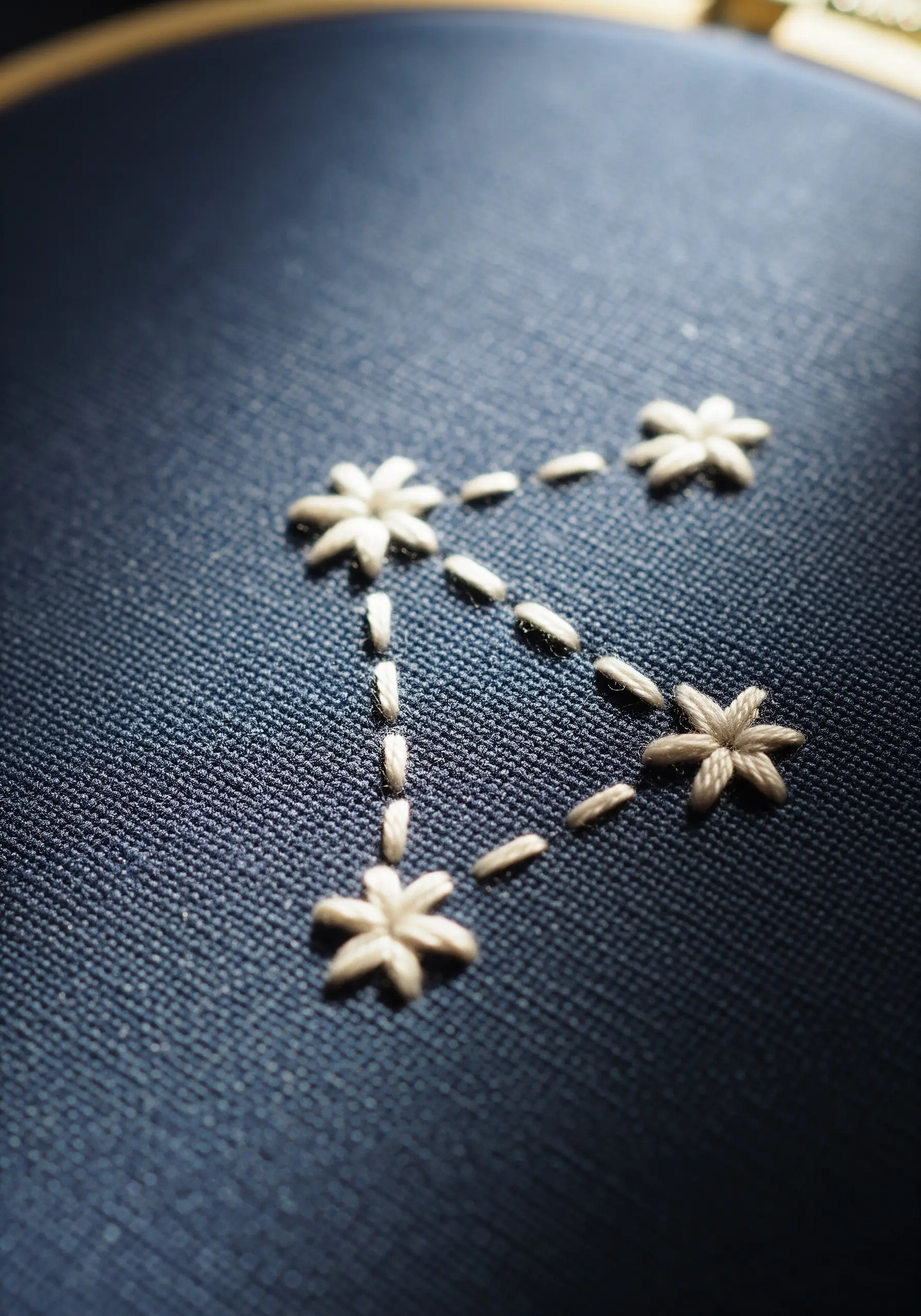 A minimalist constellation embroidered with white thread on dark blue fabric.