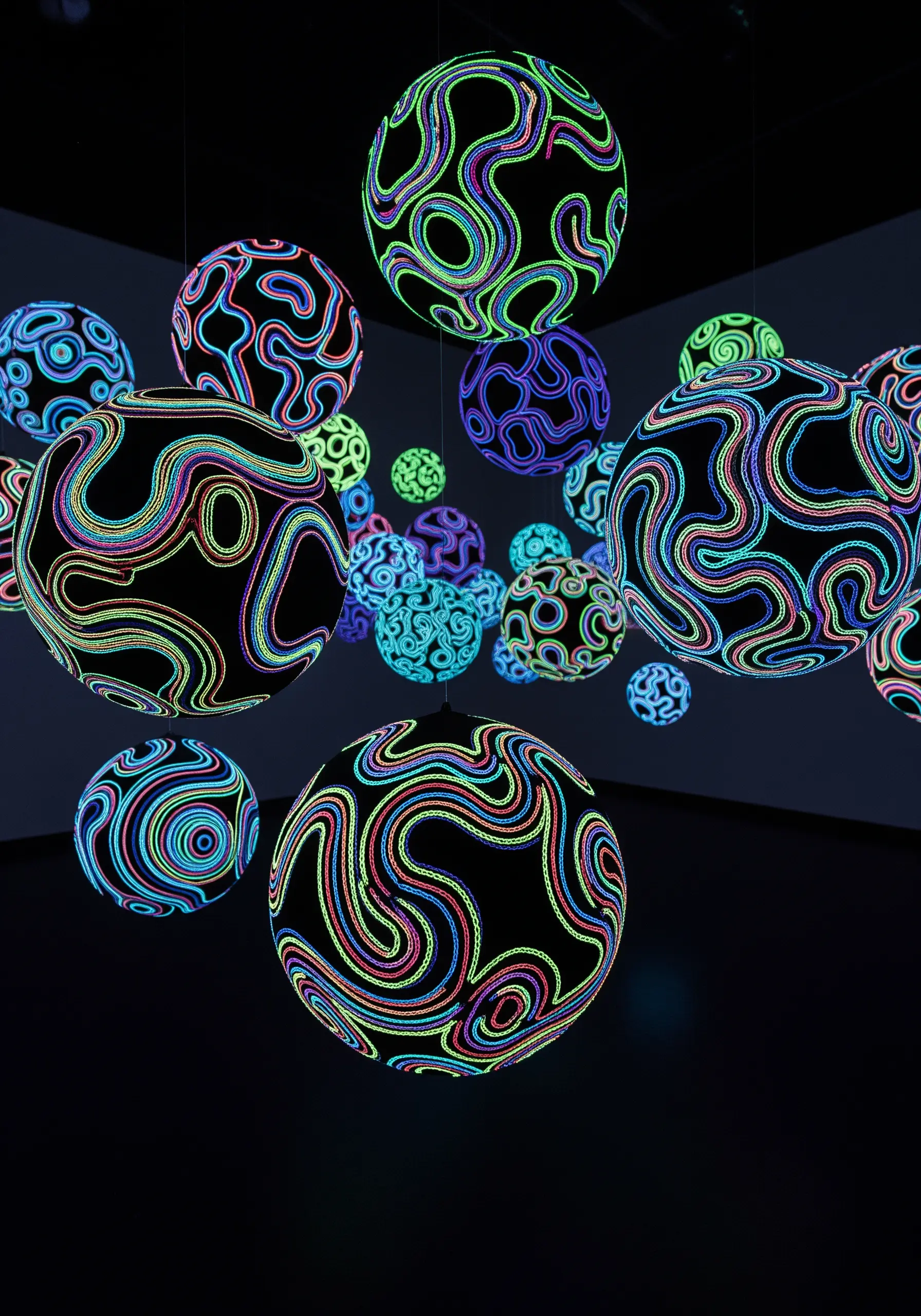 Black spheres covered in glowing, UV-reactive embroidered lines in a dark space.