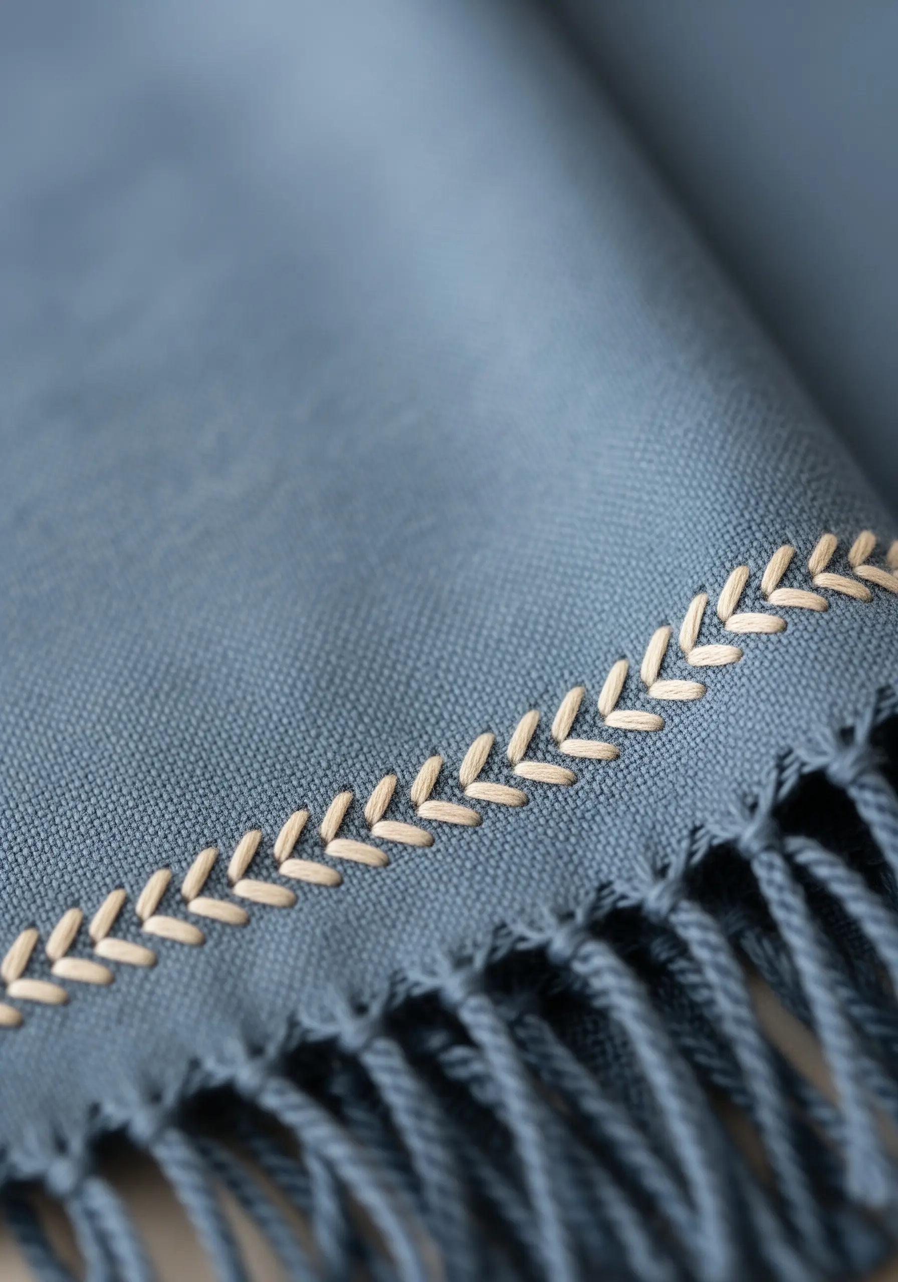 A decorative border of fly stitches resembling leaves along the edge of a blue scarf.