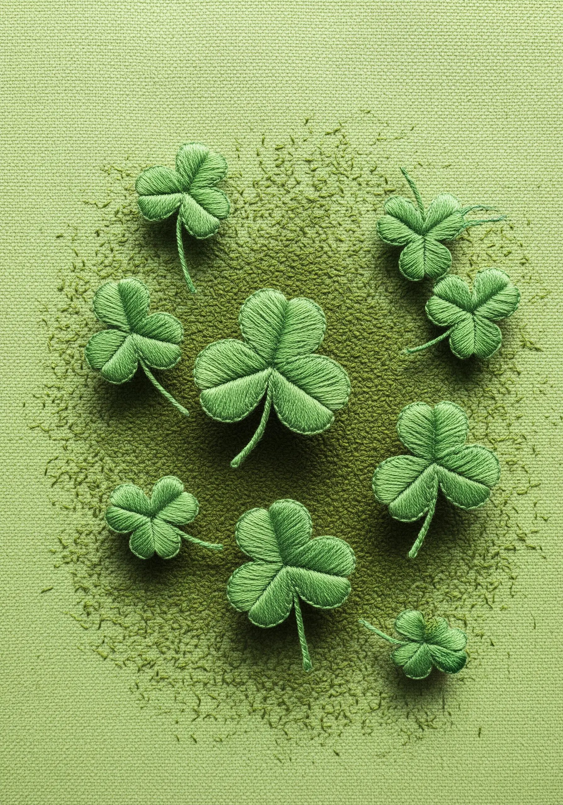 Puffy embroidered clovers on a green background with a textured, scattered-stitch shadow.