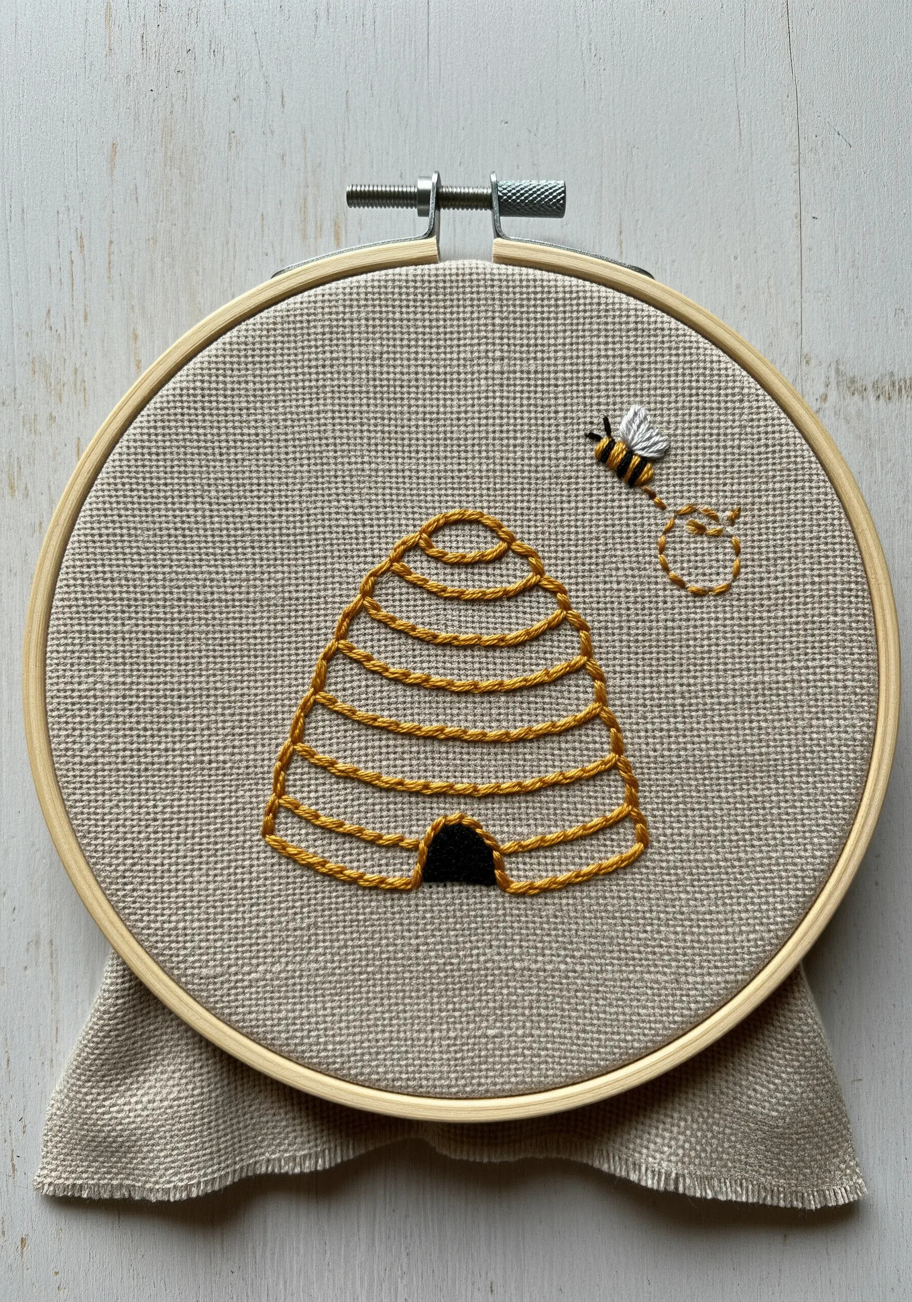 A minimalist beehive embroidery created with simple coiled outlines in yellow thread.