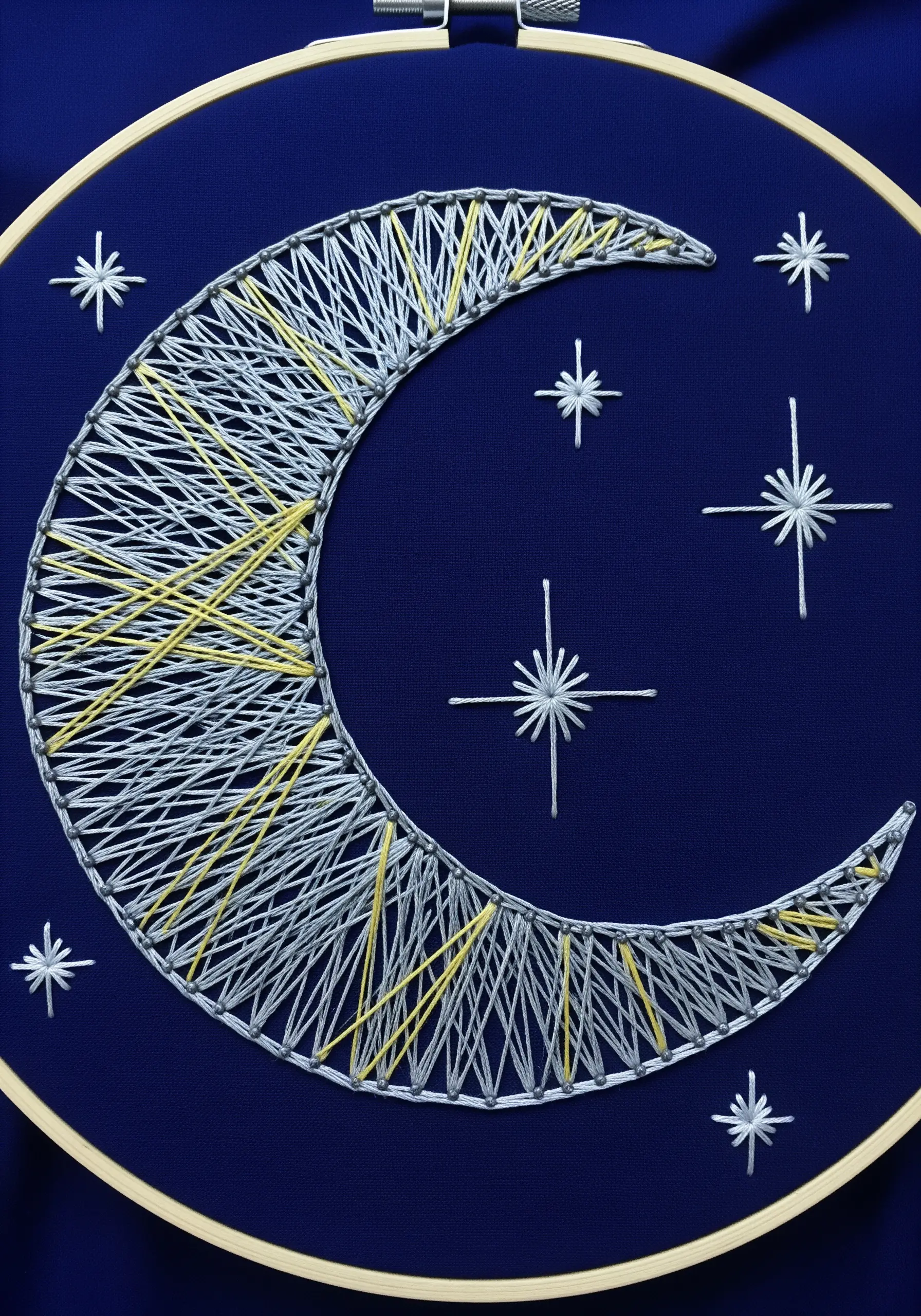 Embroidery of a crescent moon and stars using open, crisscrossing white and yellow stitches