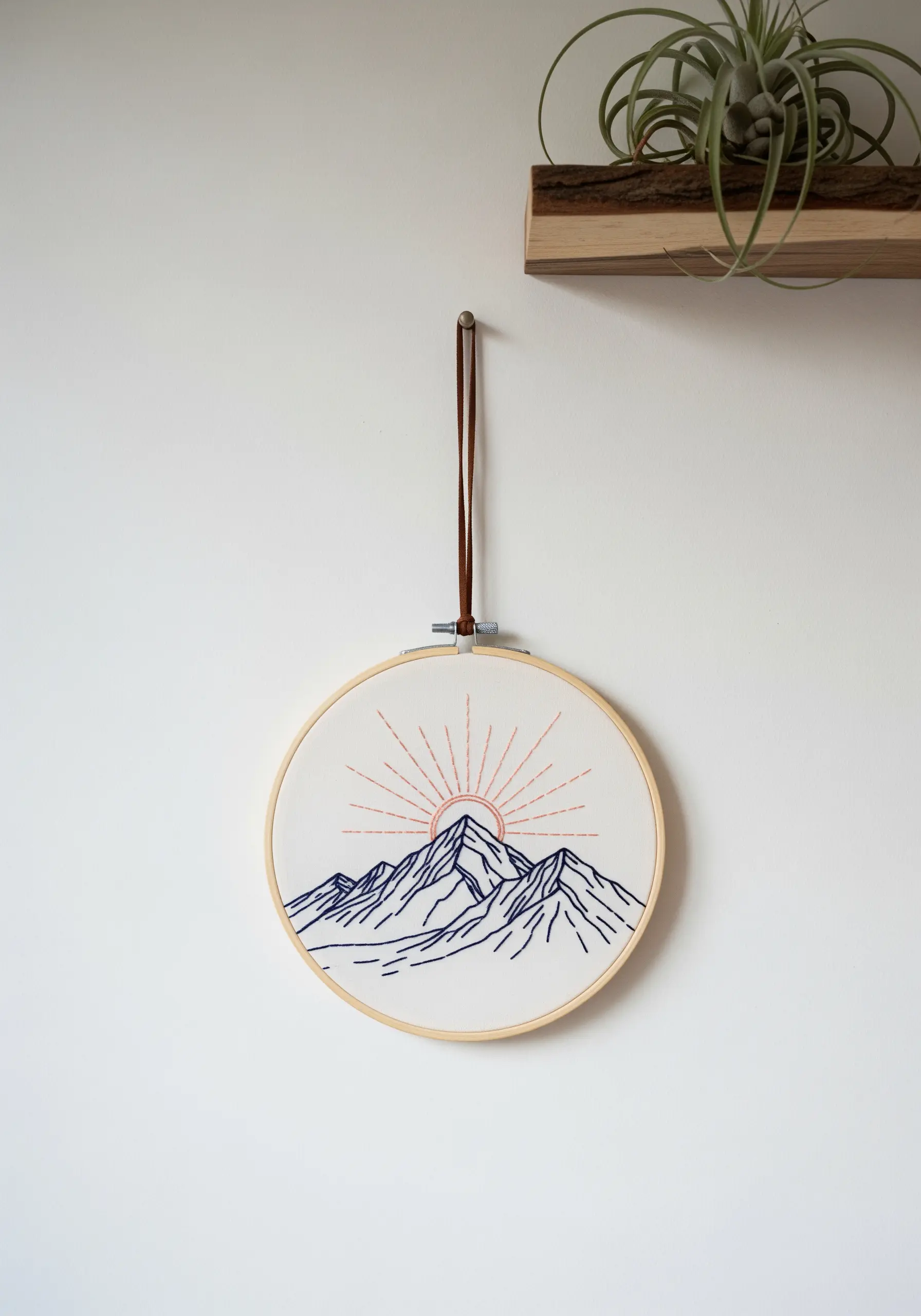 Minimalist embroidery of a mountain range with a rising sun in a simple line art style.