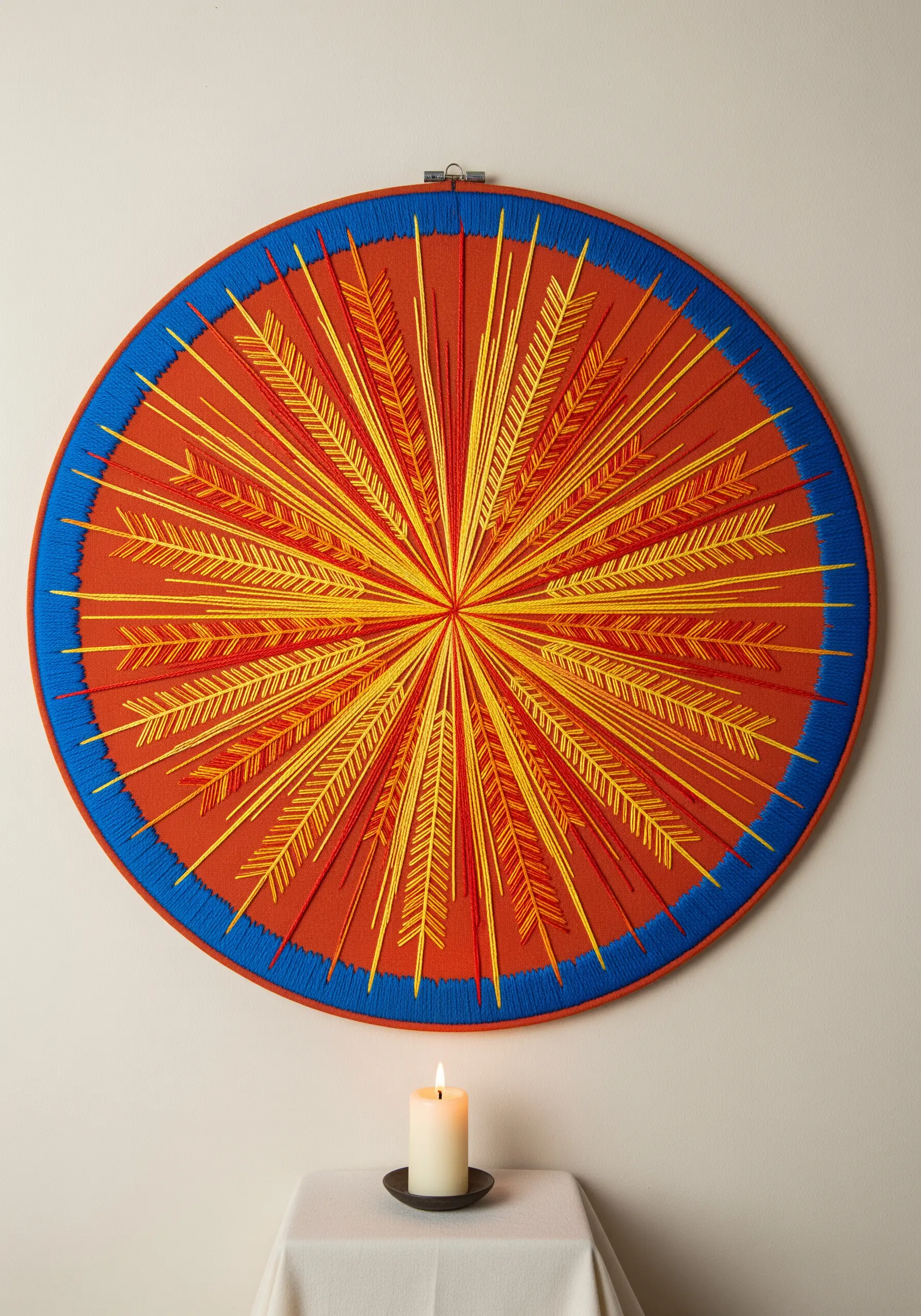 A sunburst mandala with radiating stitches in red and yellow, framed in a blue yarn-wrapped hoop.
