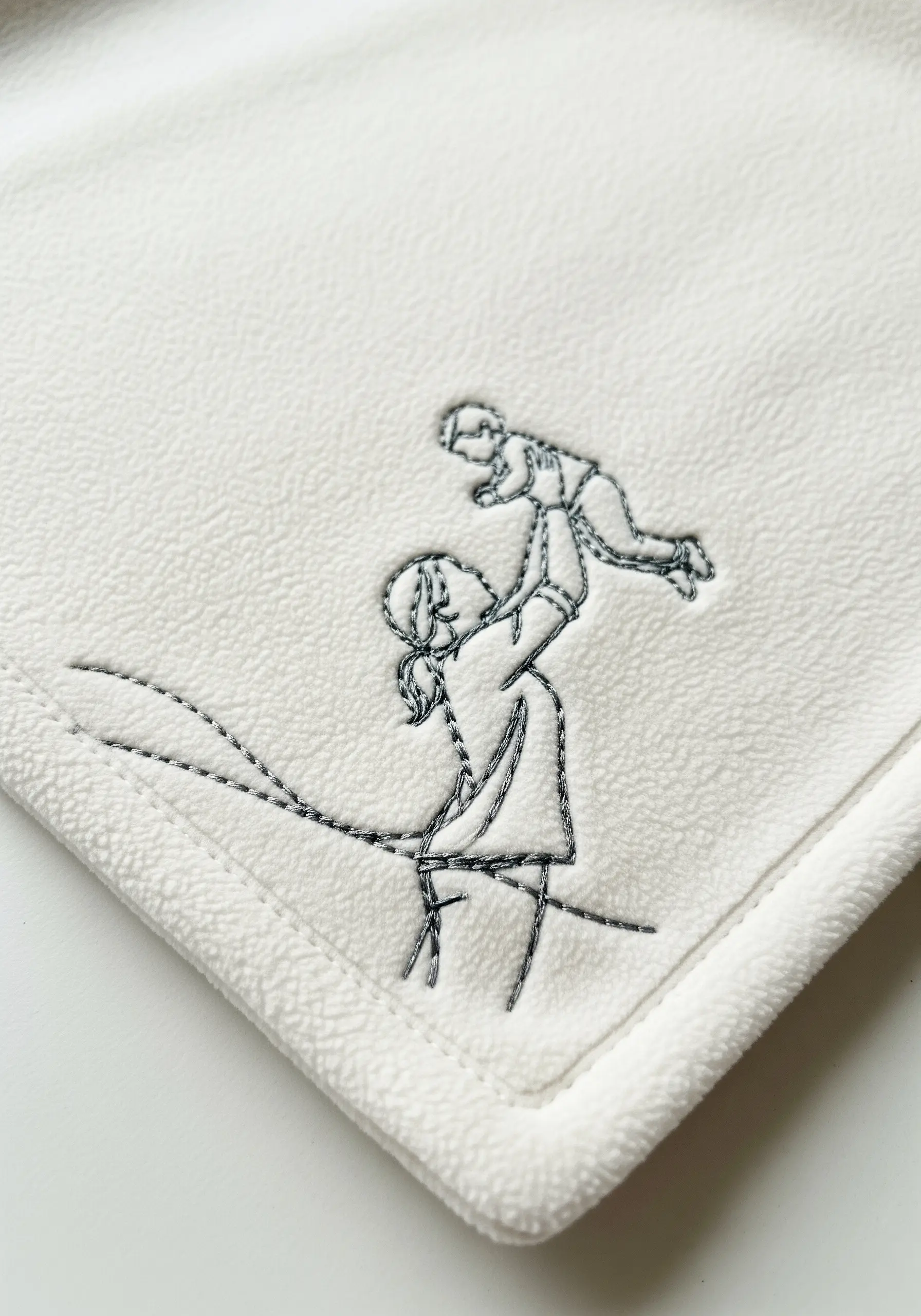 A close-up of a mother-and-child line art motif stitched in black on a cream fleece blanket.