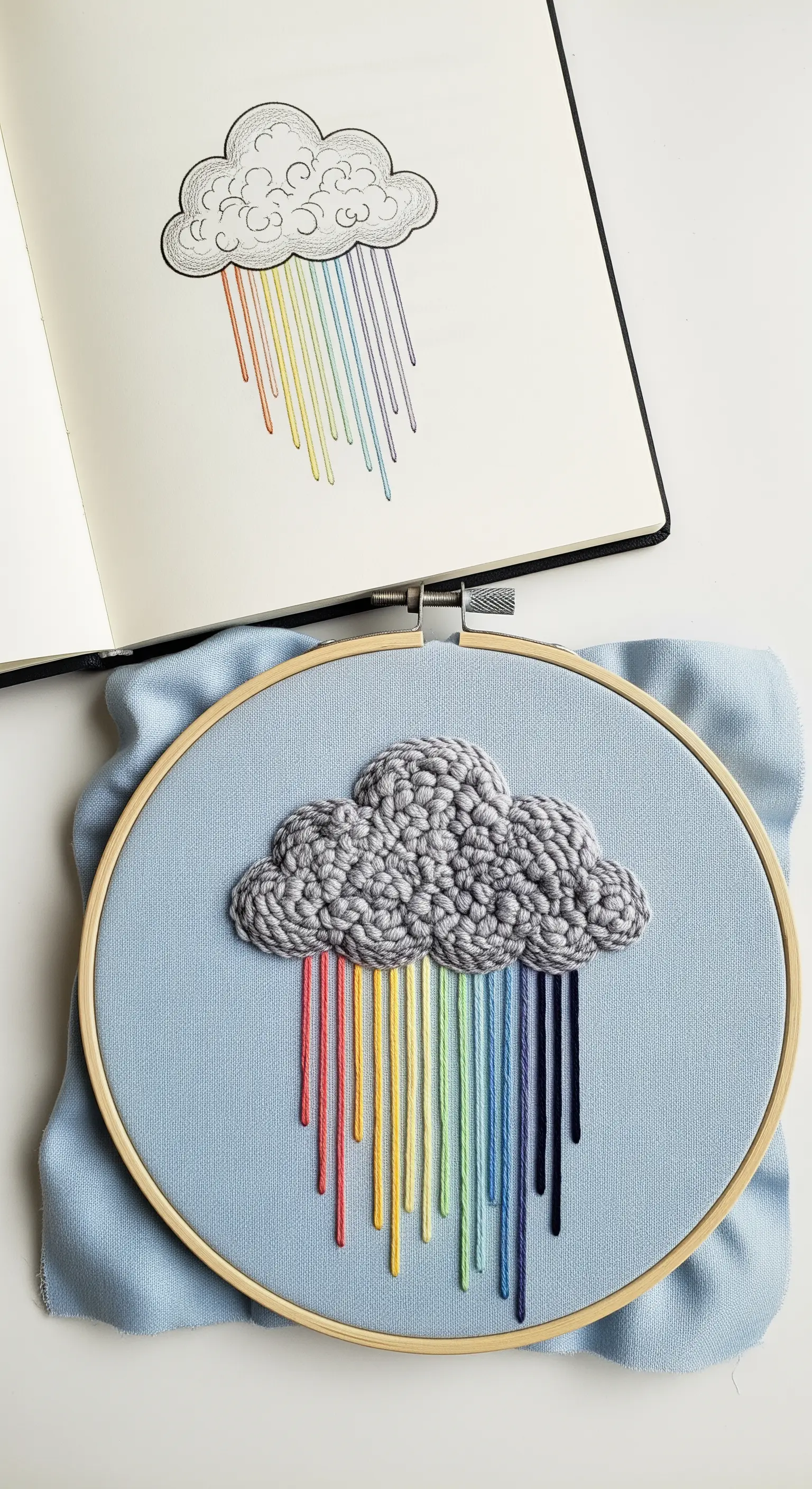 An embroidered cloud of gray French knots with smooth, straight-stitch rainbow rain.