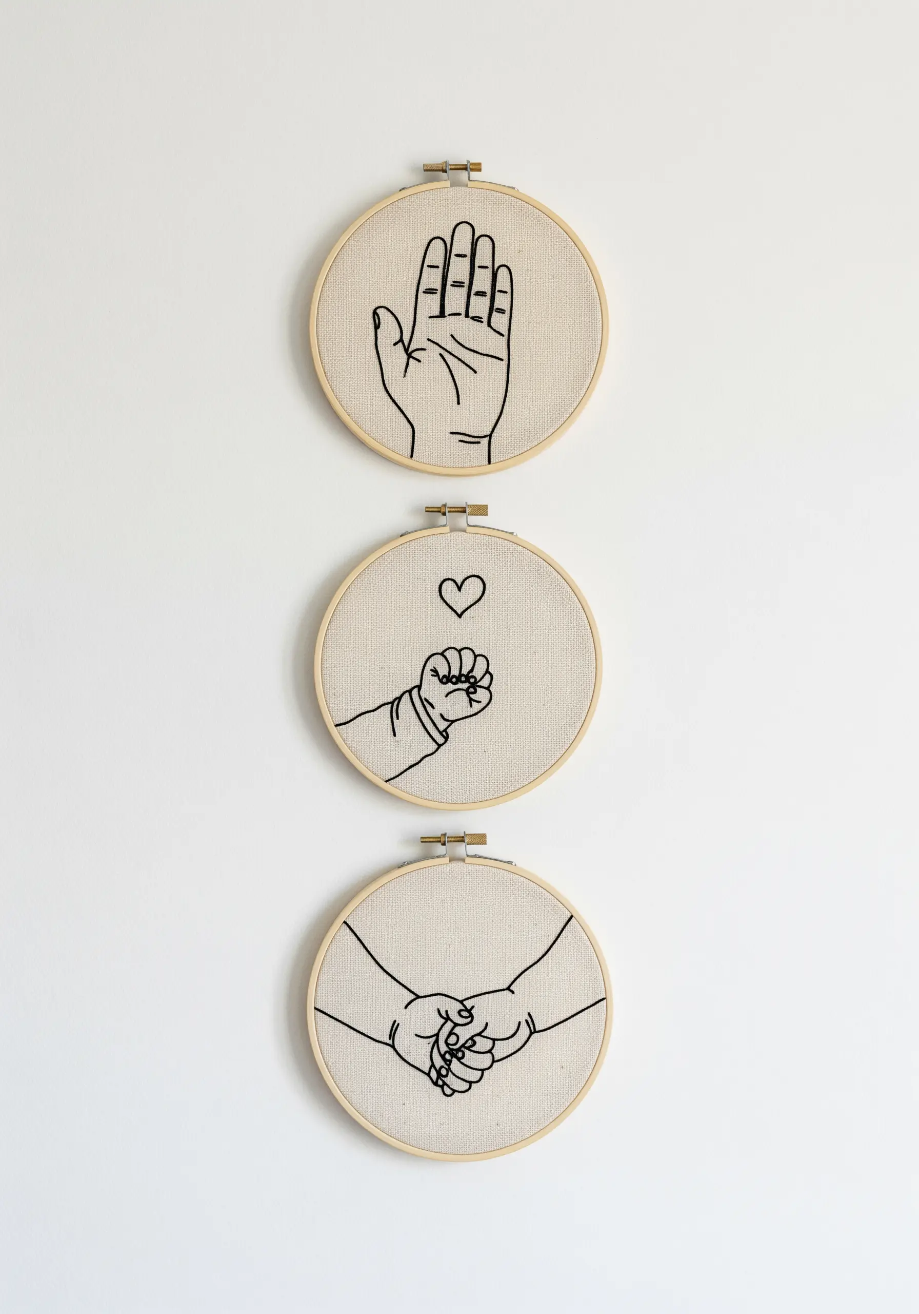 A set of three embroidery hoops depicting hands, telling a story of connection.