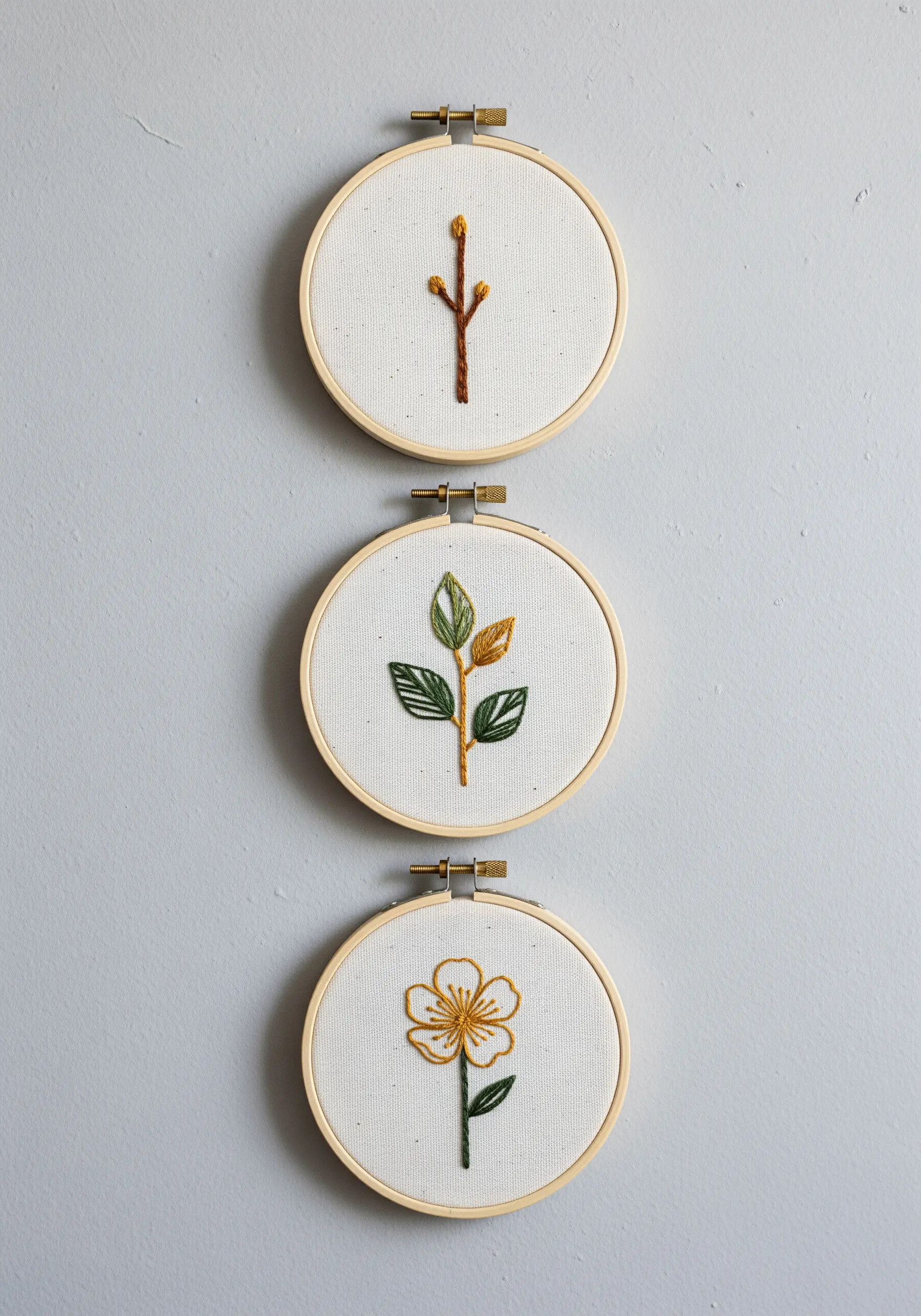Triptych of small embroidery hoops showing the growth stages of a flower.