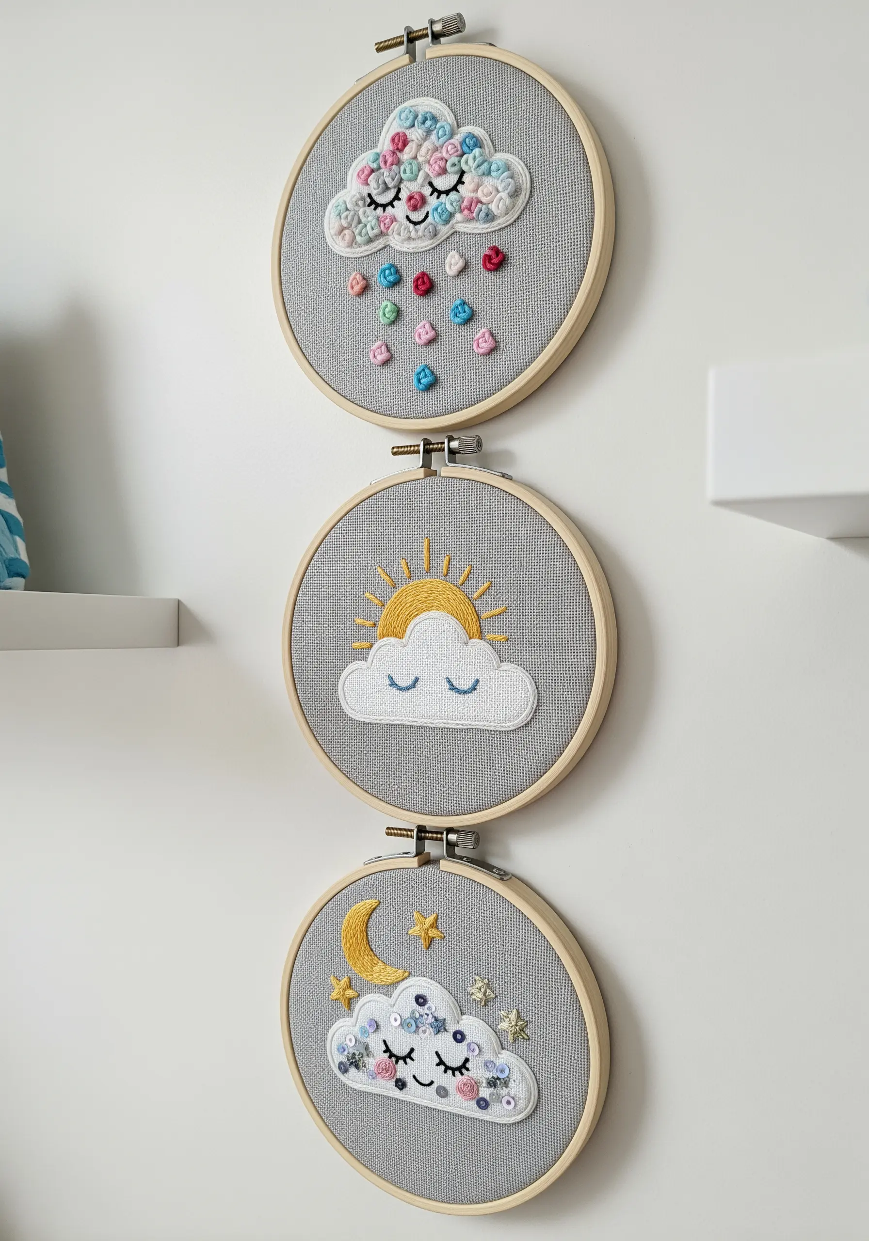Three small embroidery hoops depicting weather scenes: rain, sun, and moon.