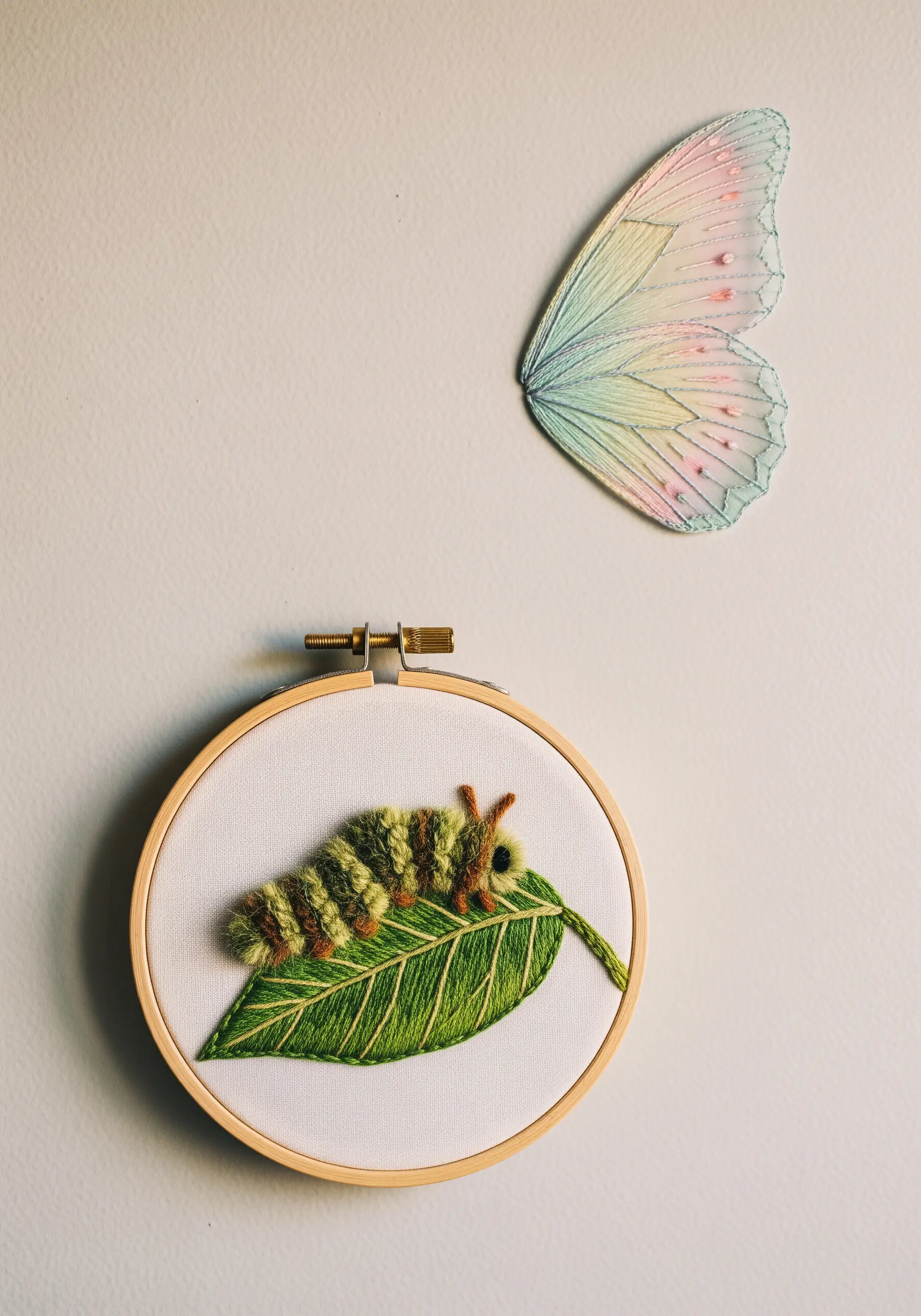 Dimensional caterpillar on a leaf in a hoop, with a separate translucent wing nearby.