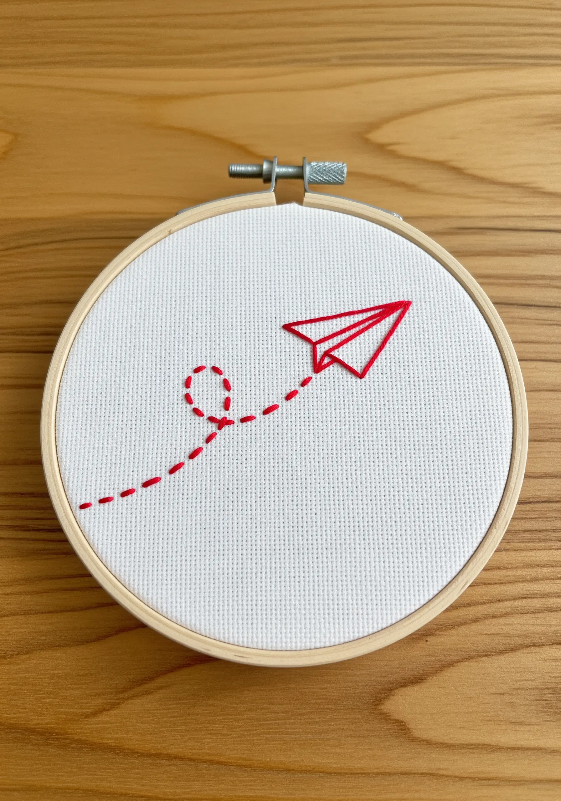 A red paper airplane with a dotted flight path embroidered on white Aida cloth.