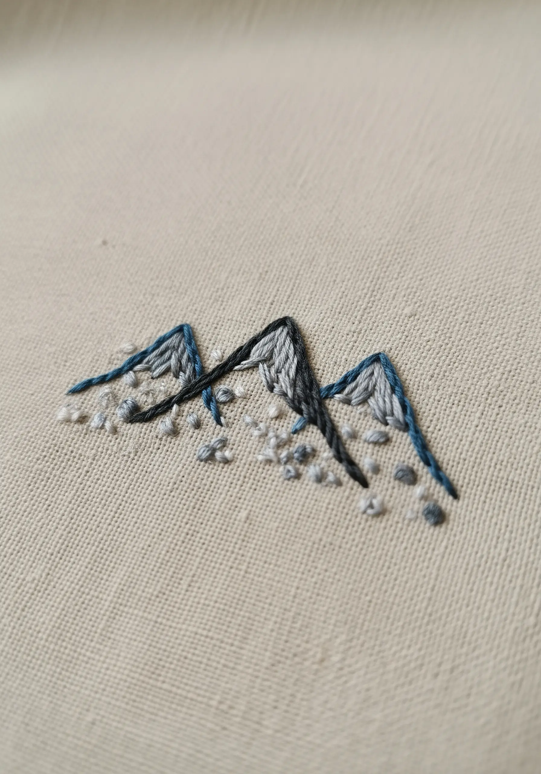 Minimalist mountain embroidery with textural long-and-short stitch and French knots.