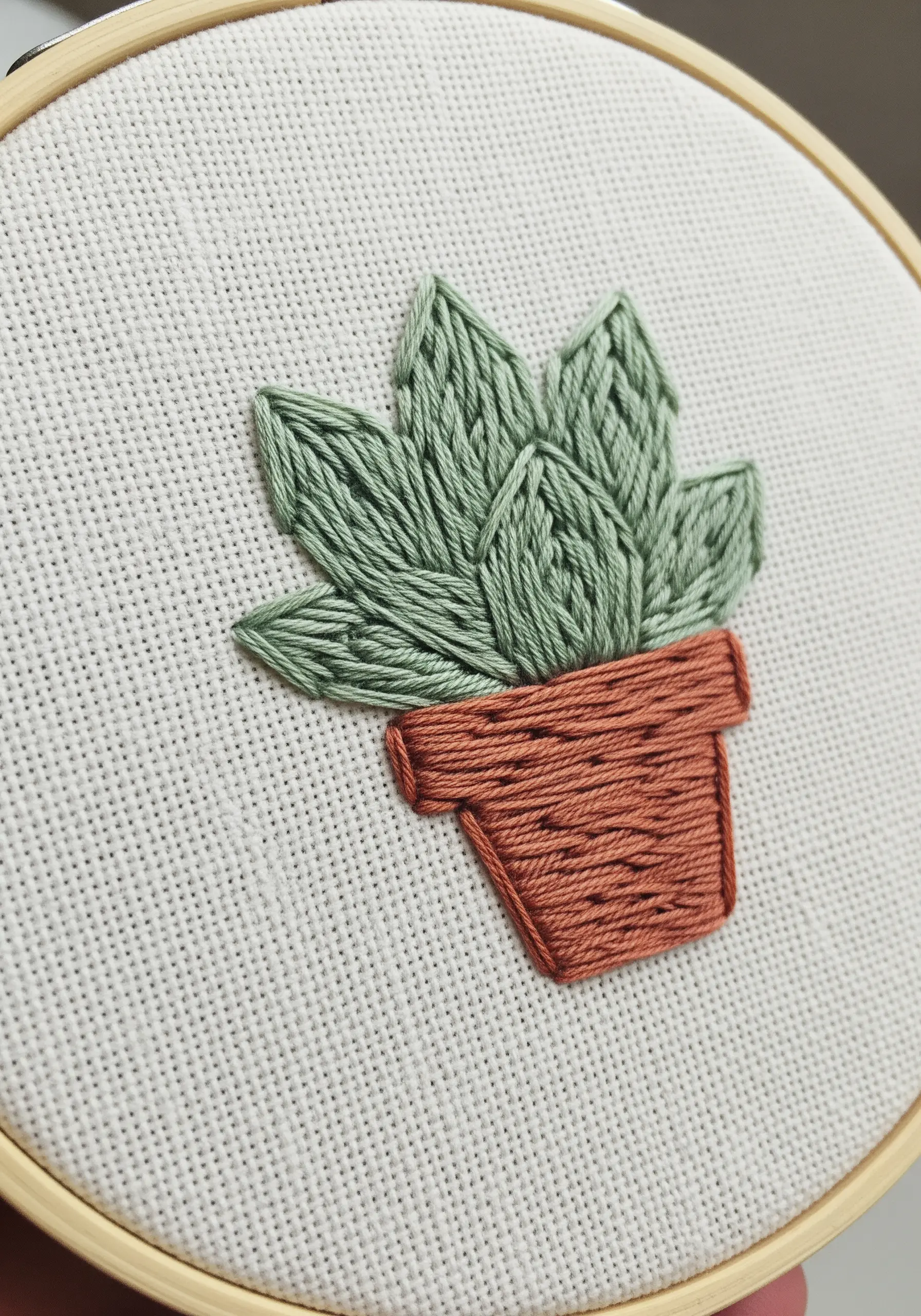 Small embroidered potted succulent with green fishbone stitch leaves.