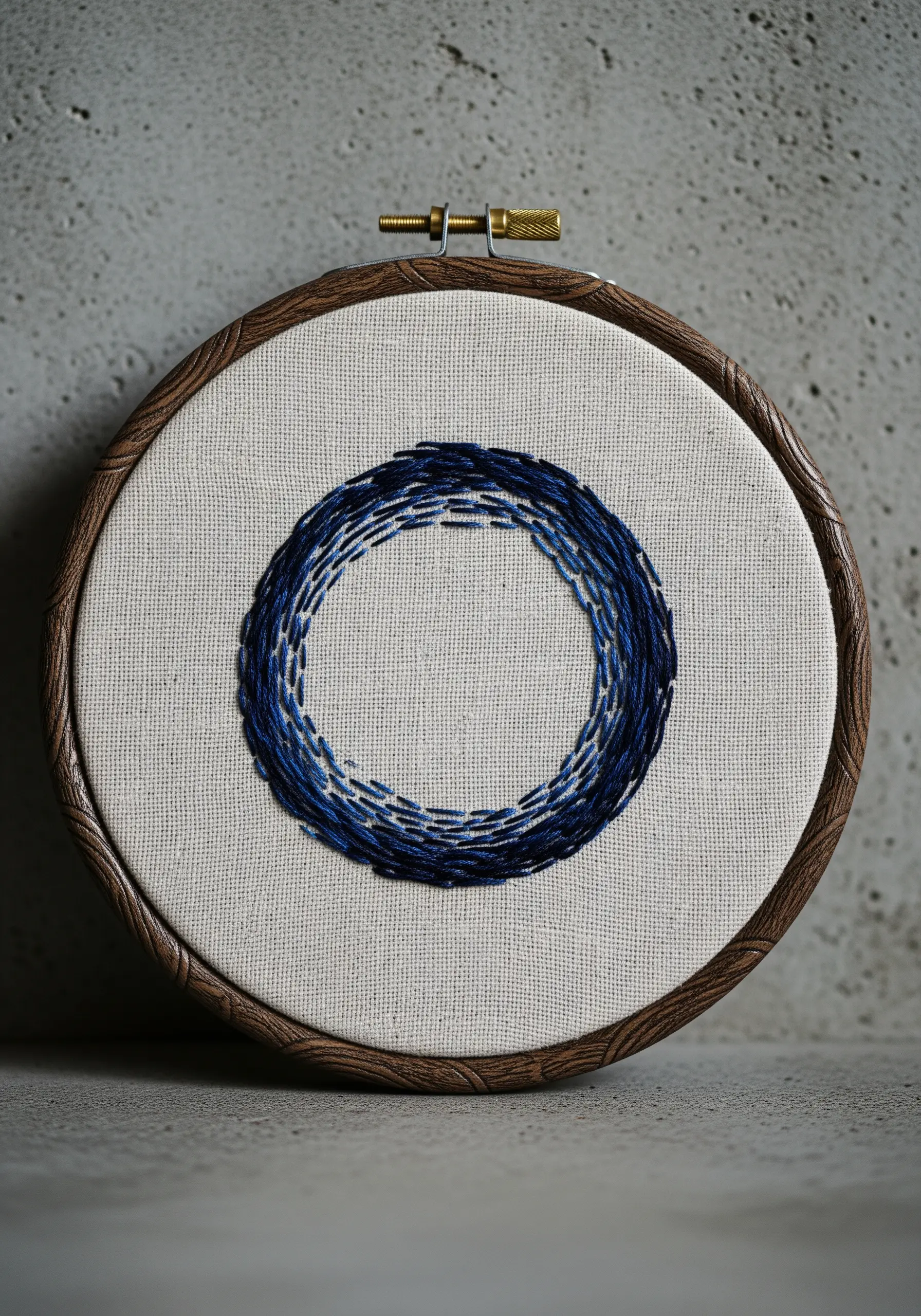 A textured embroidered circle with layered blue stitches in a dark wood hoop.