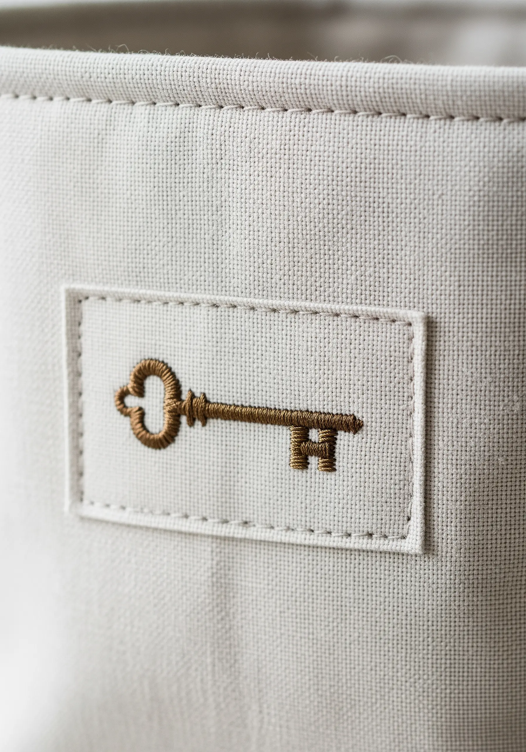 An embroidered antique key on a fabric patch stitched onto a canvas storage bin.