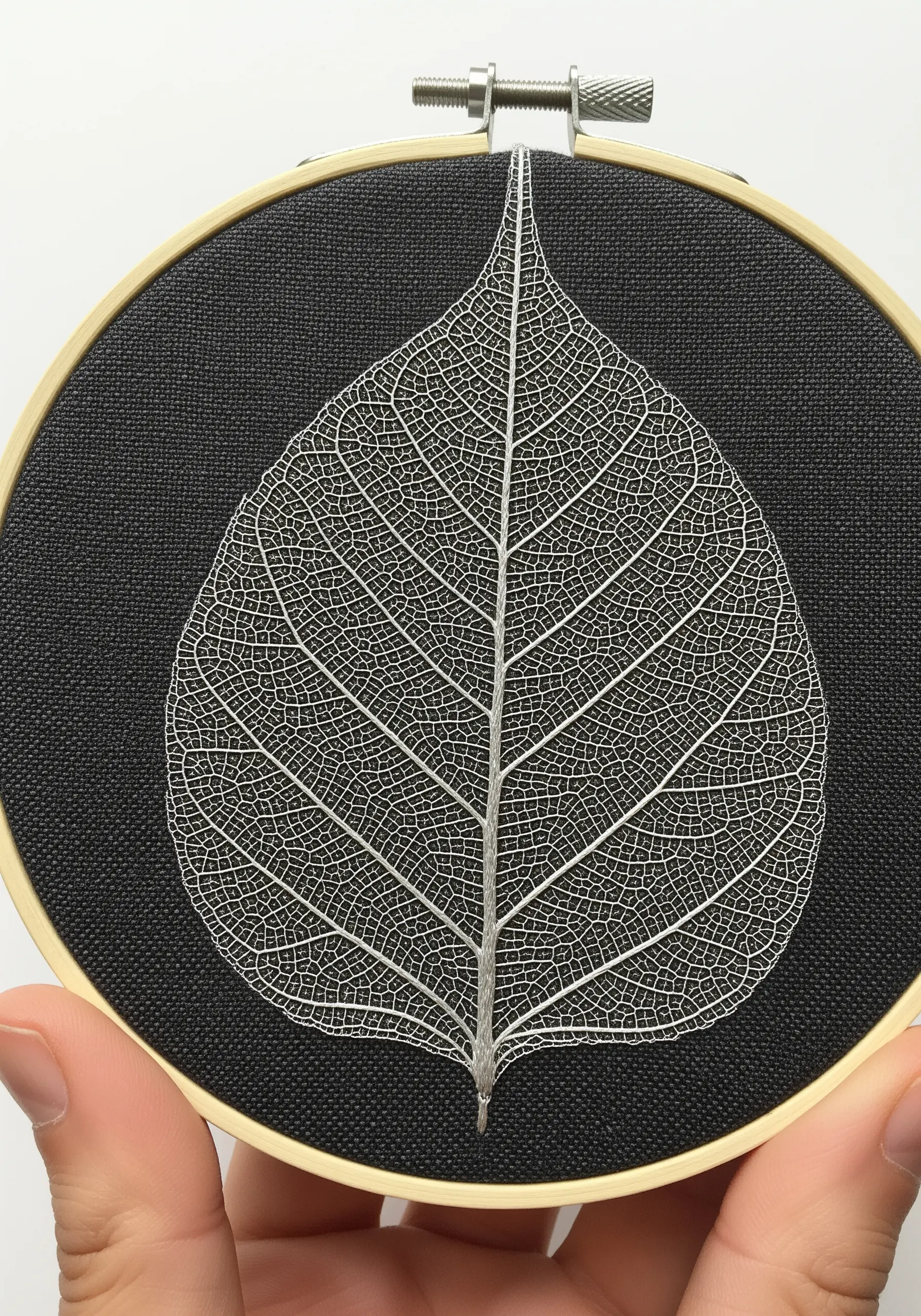 A hyper-realistic skeleton leaf embroidered with fine white thread on black fabric.