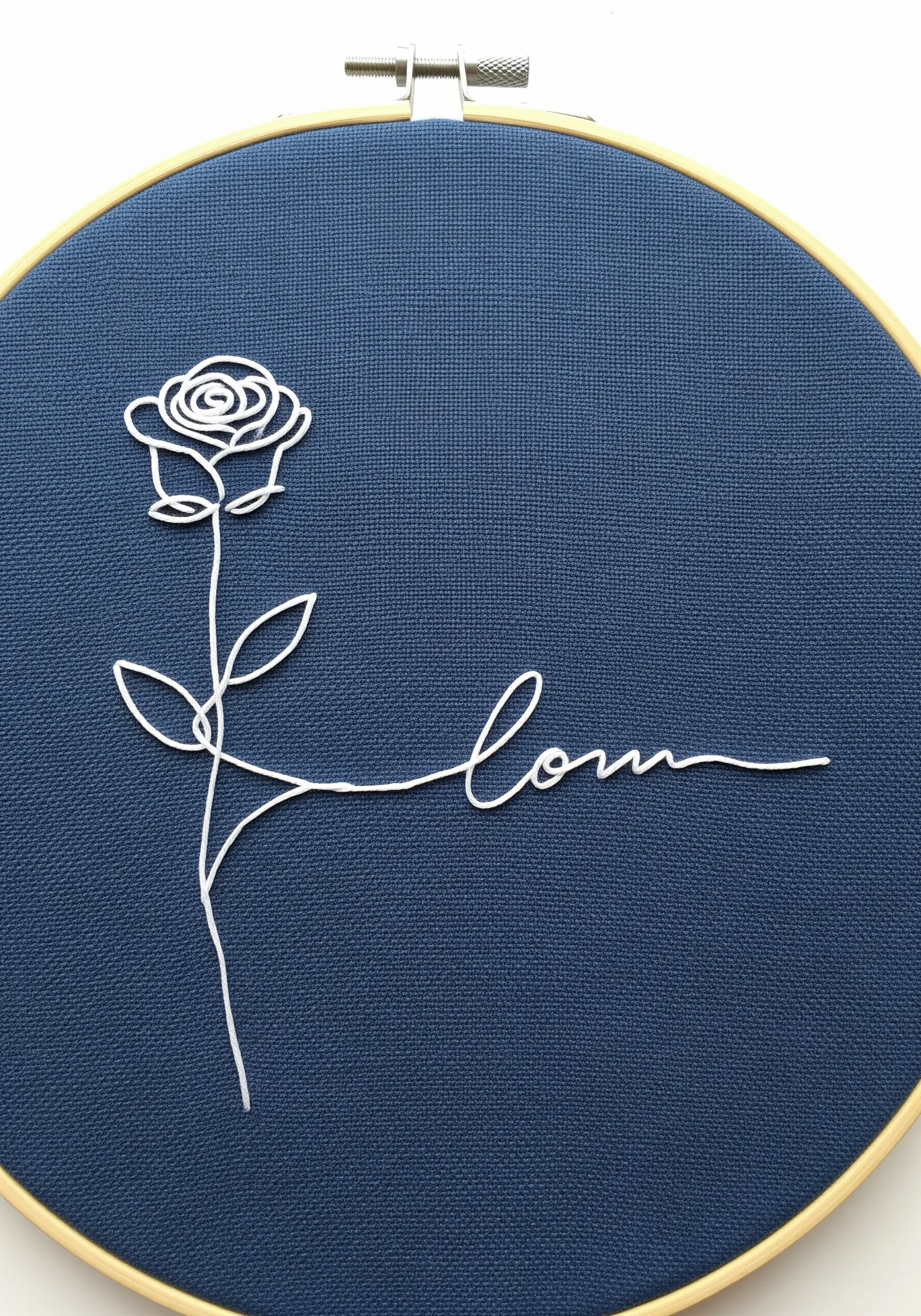 A minimalist single-line embroidery of a rose that flows into the word 'love.'