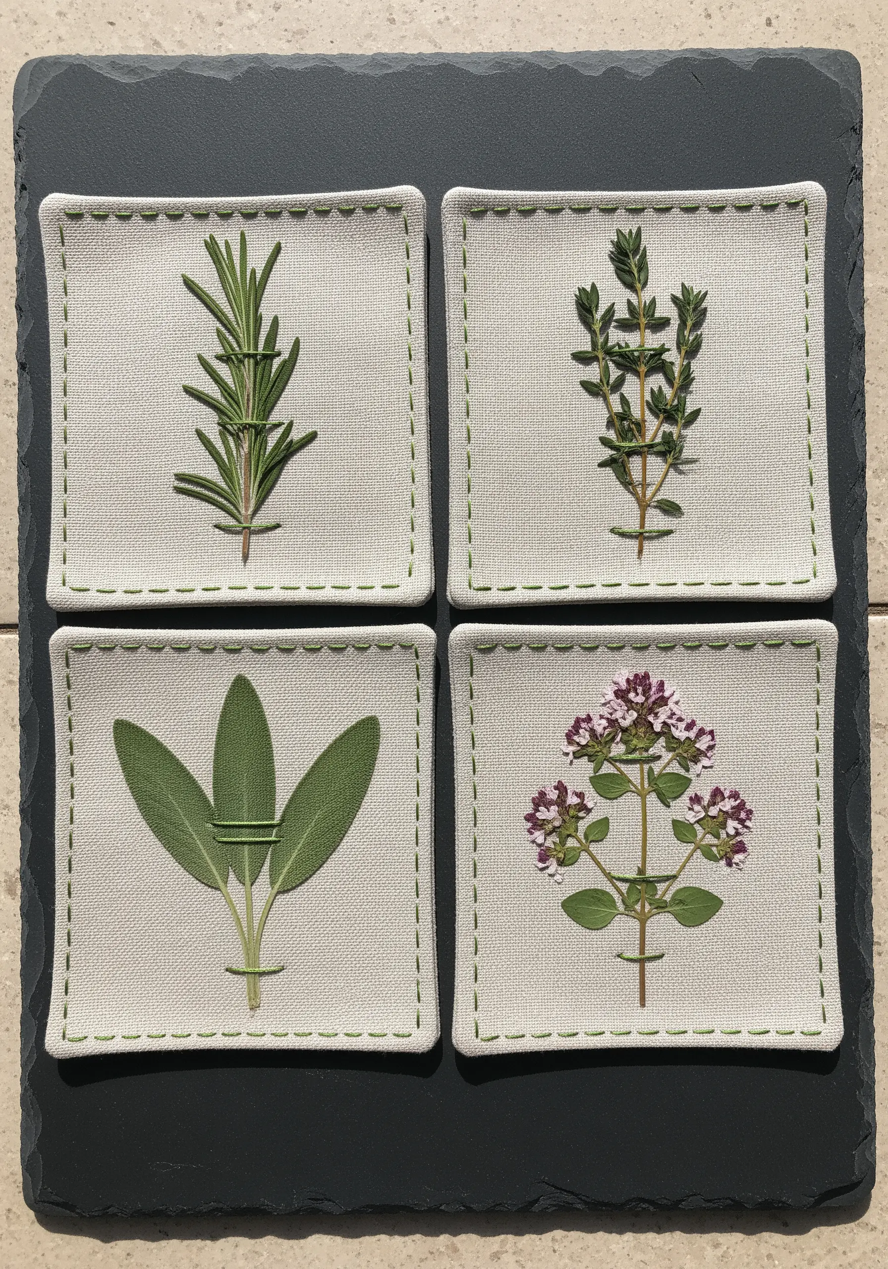 Fabric coasters, each featuring a different pressed herb secured with simple thread stitches.
