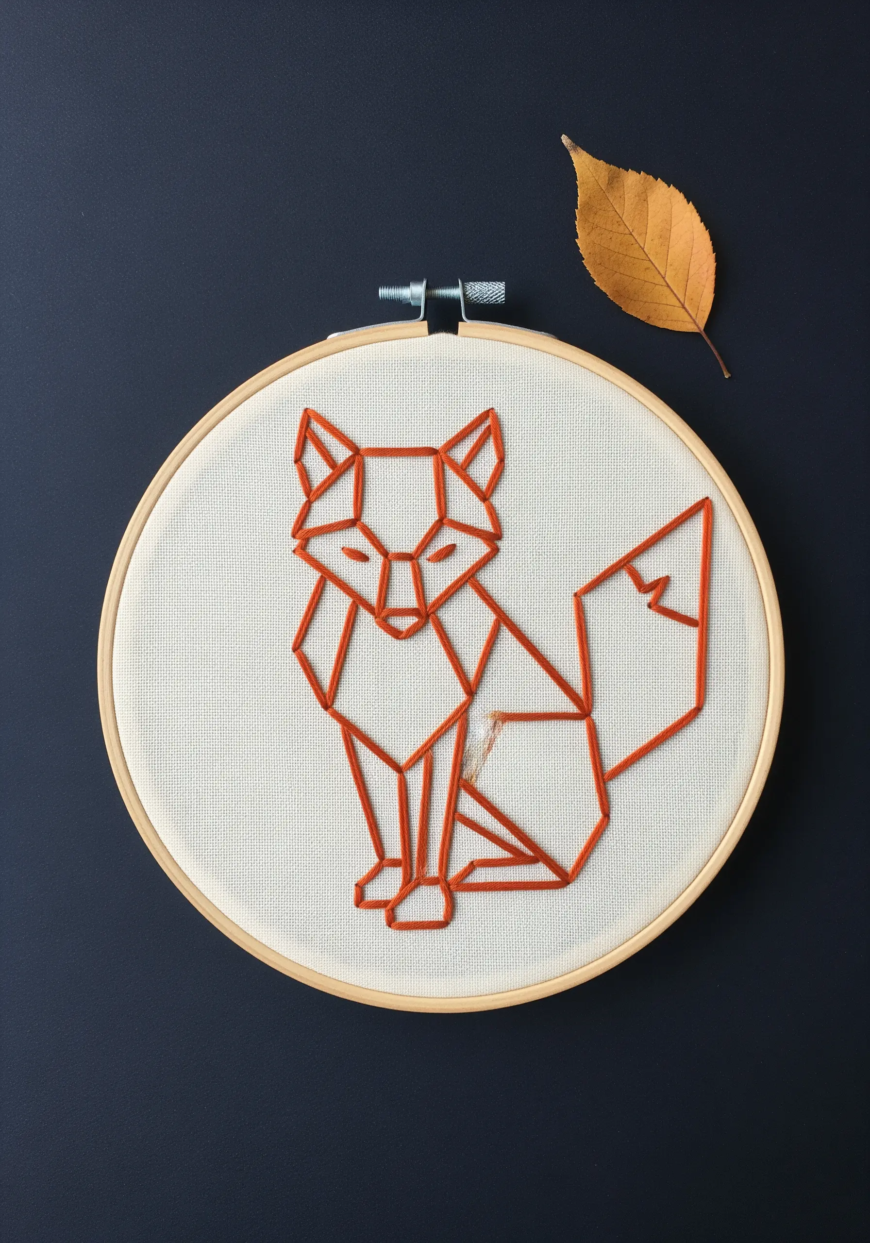 Geometric orange fox embroidered with satin stitch on off-white fabric.