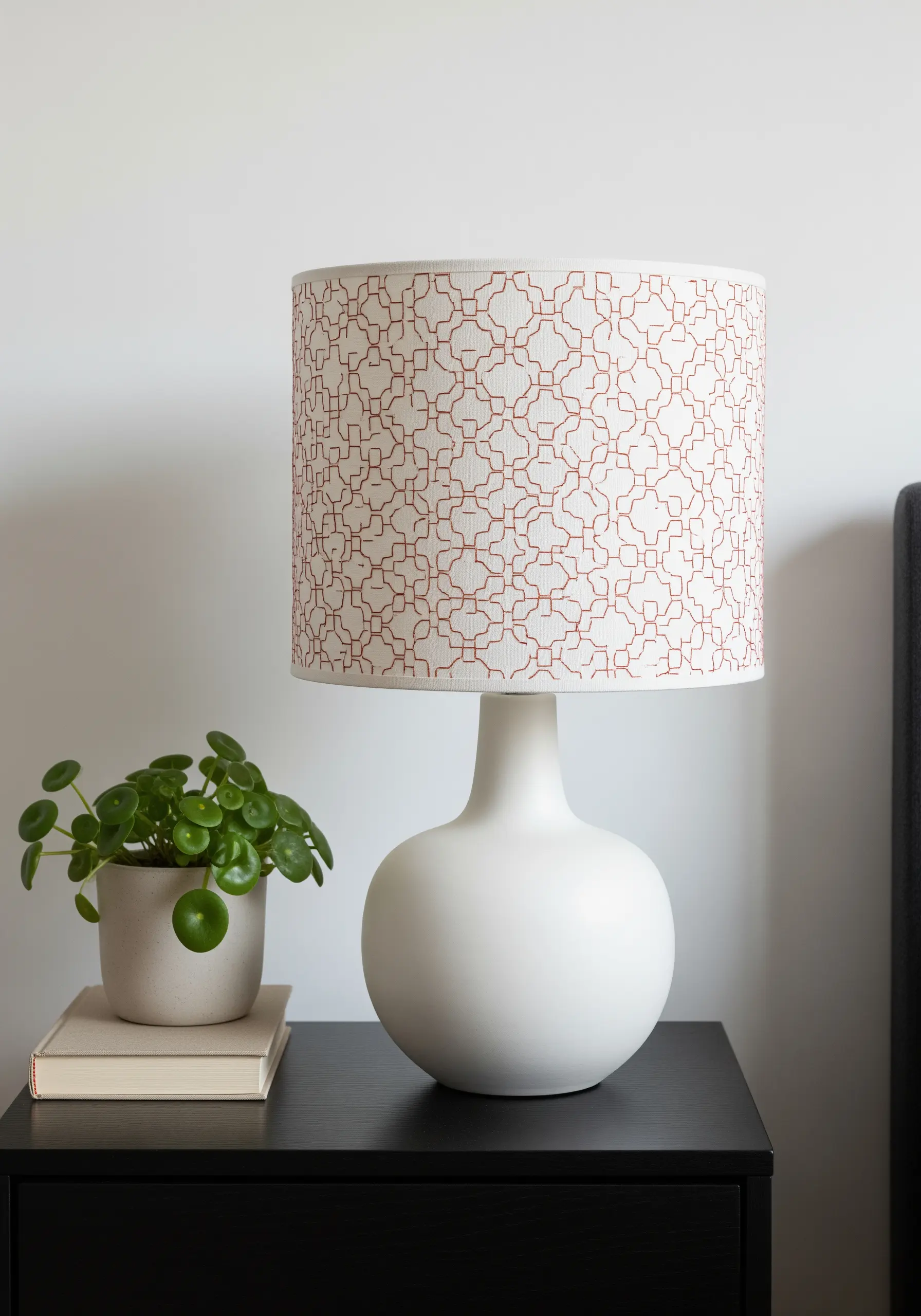 A white drum lampshade with a repeating geometric pattern embroidered in rust-colored thread.