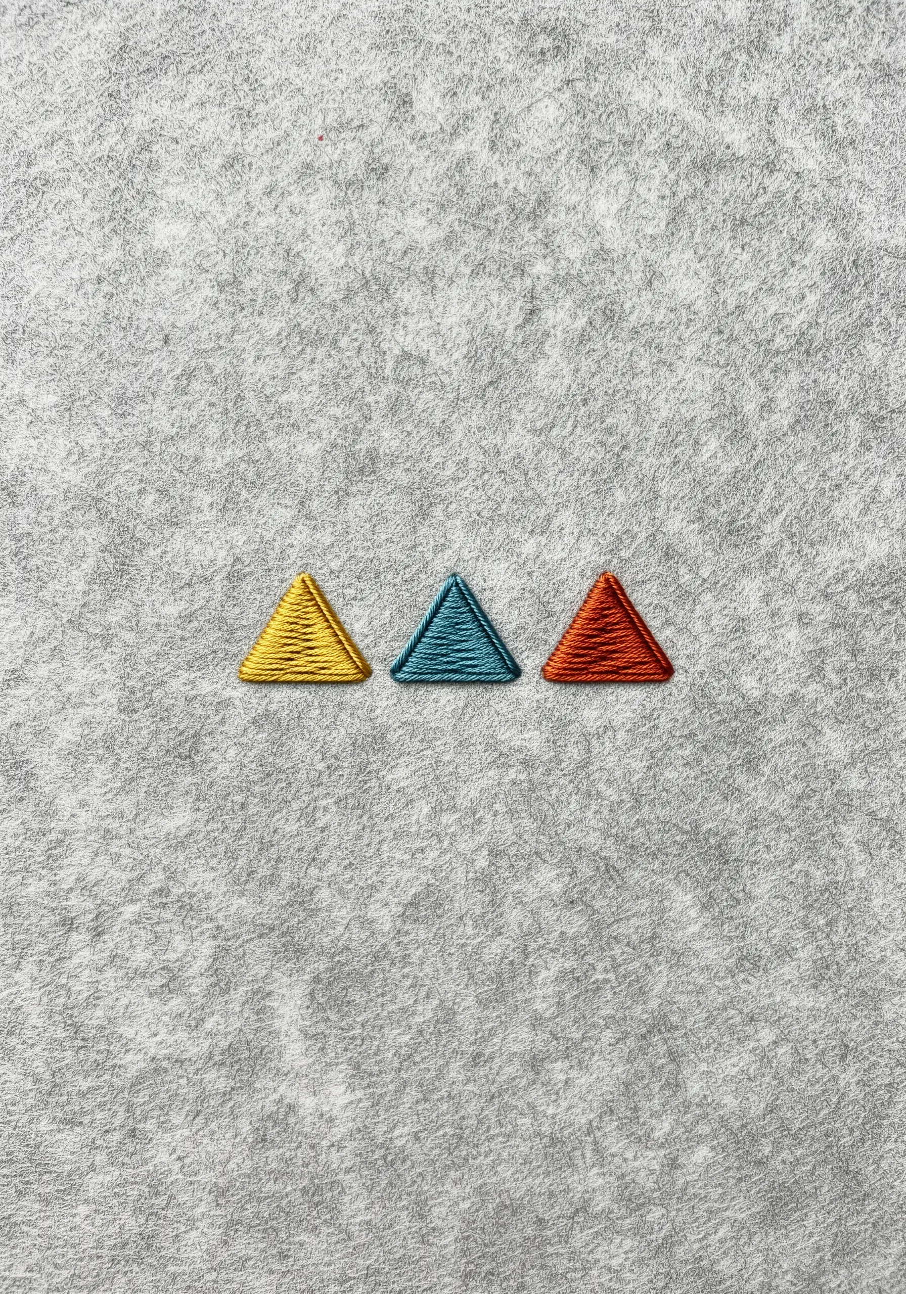 Three small, satin-stitched triangles in yellow, teal, and orange on gray felt.