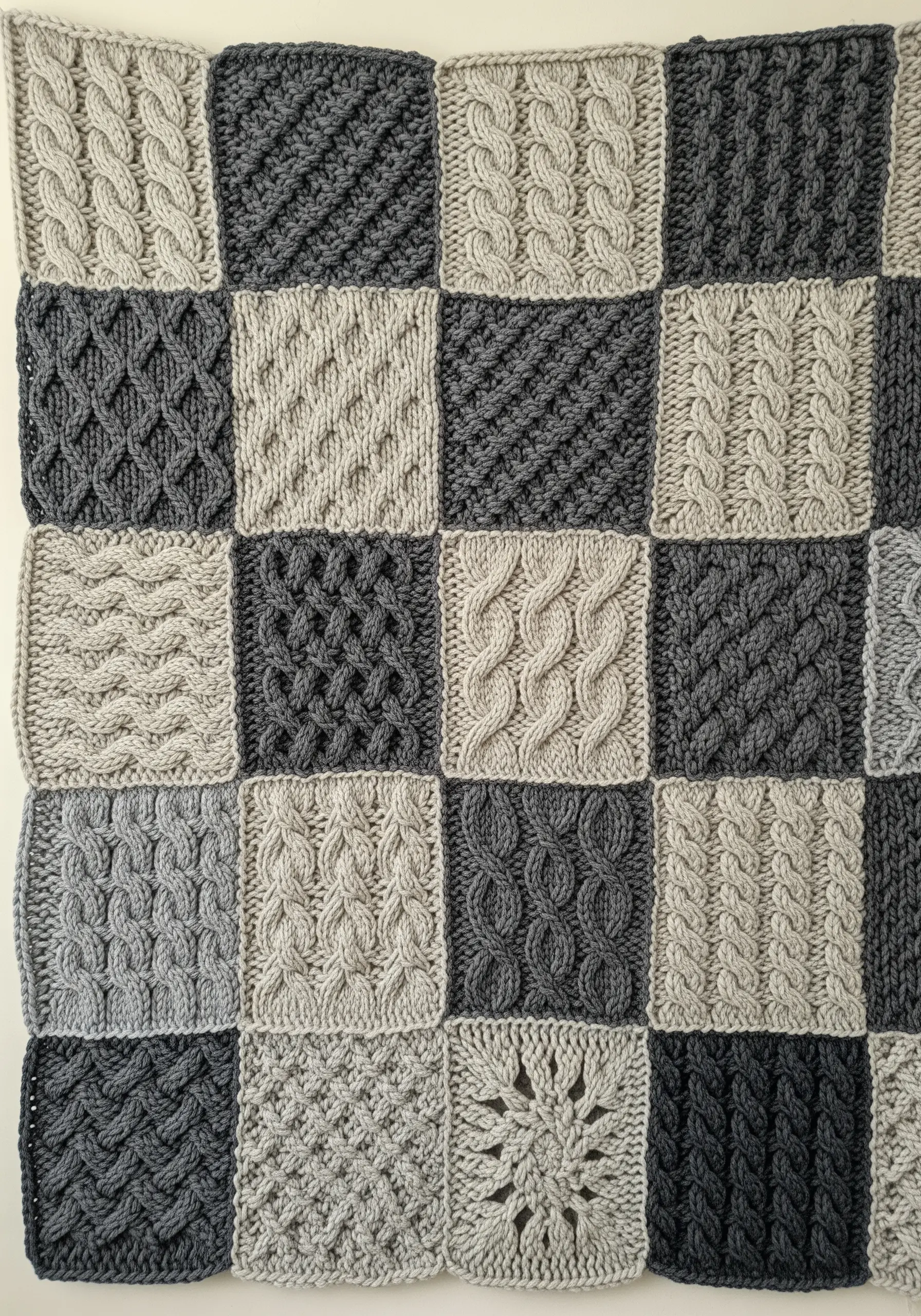 A patchwork blanket made of knitted squares in different textures and shades of grey.