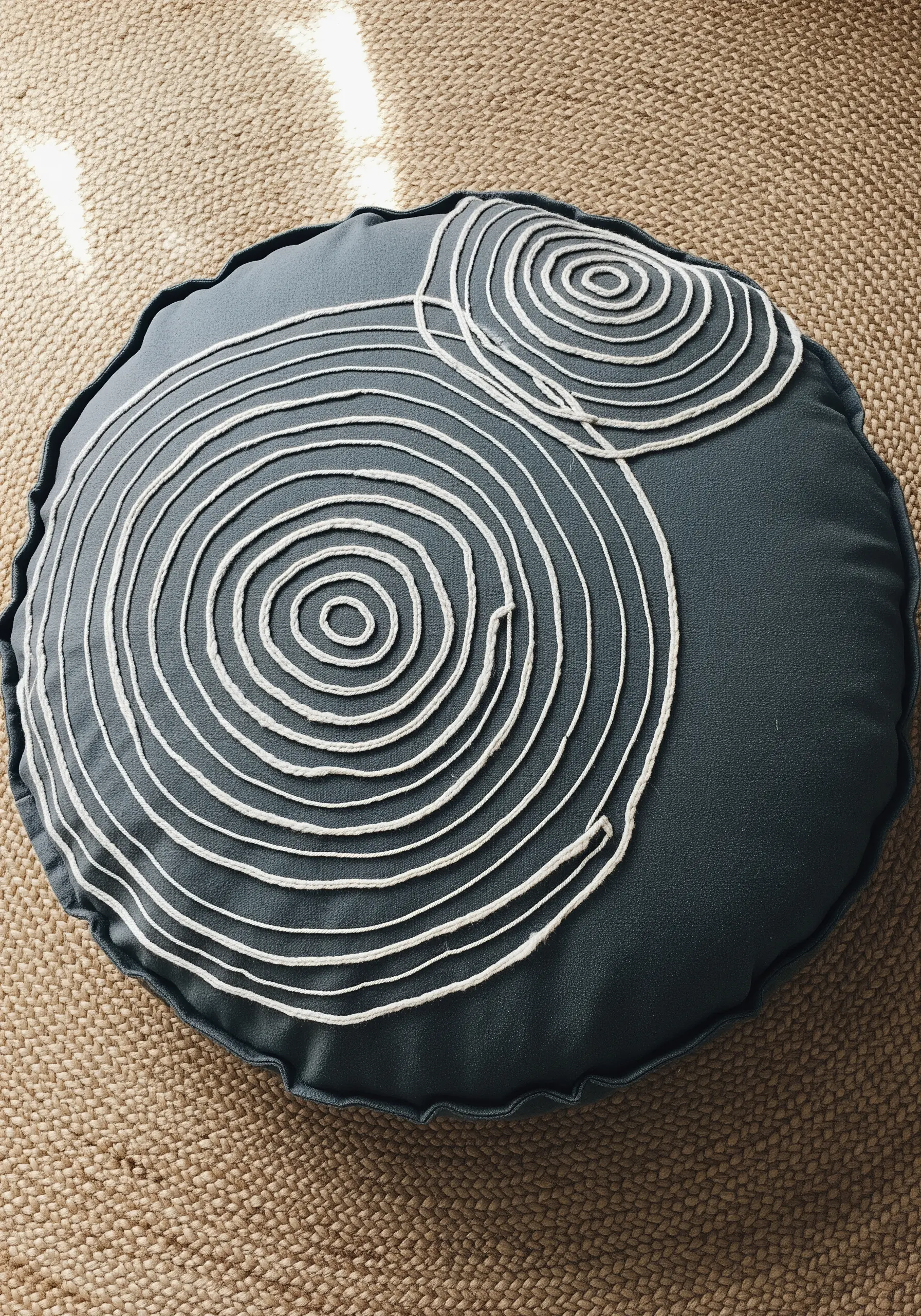 A round grey cushion with two large spirals made from couched white cord.