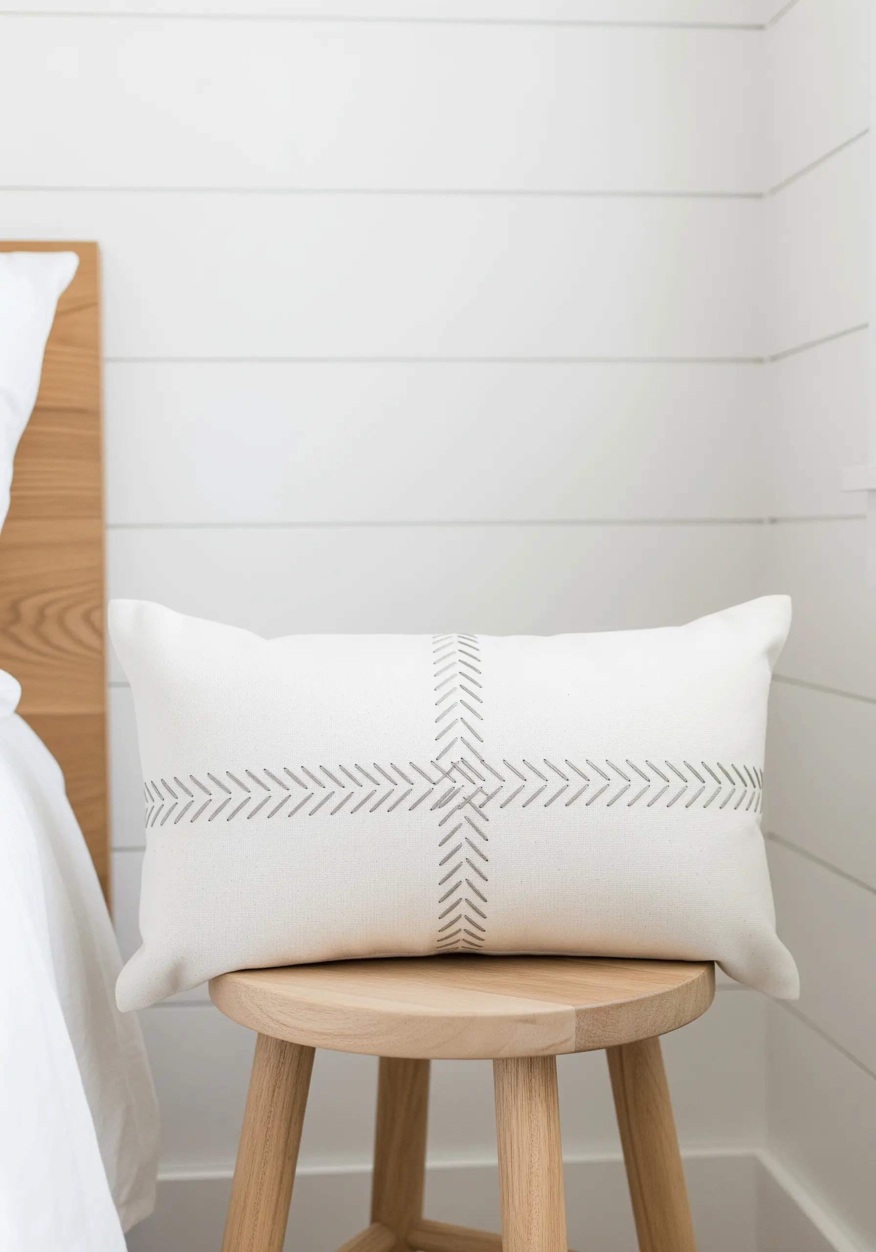A minimalist cross pattern made of grey chevron stitches on a white rectangular pillow.