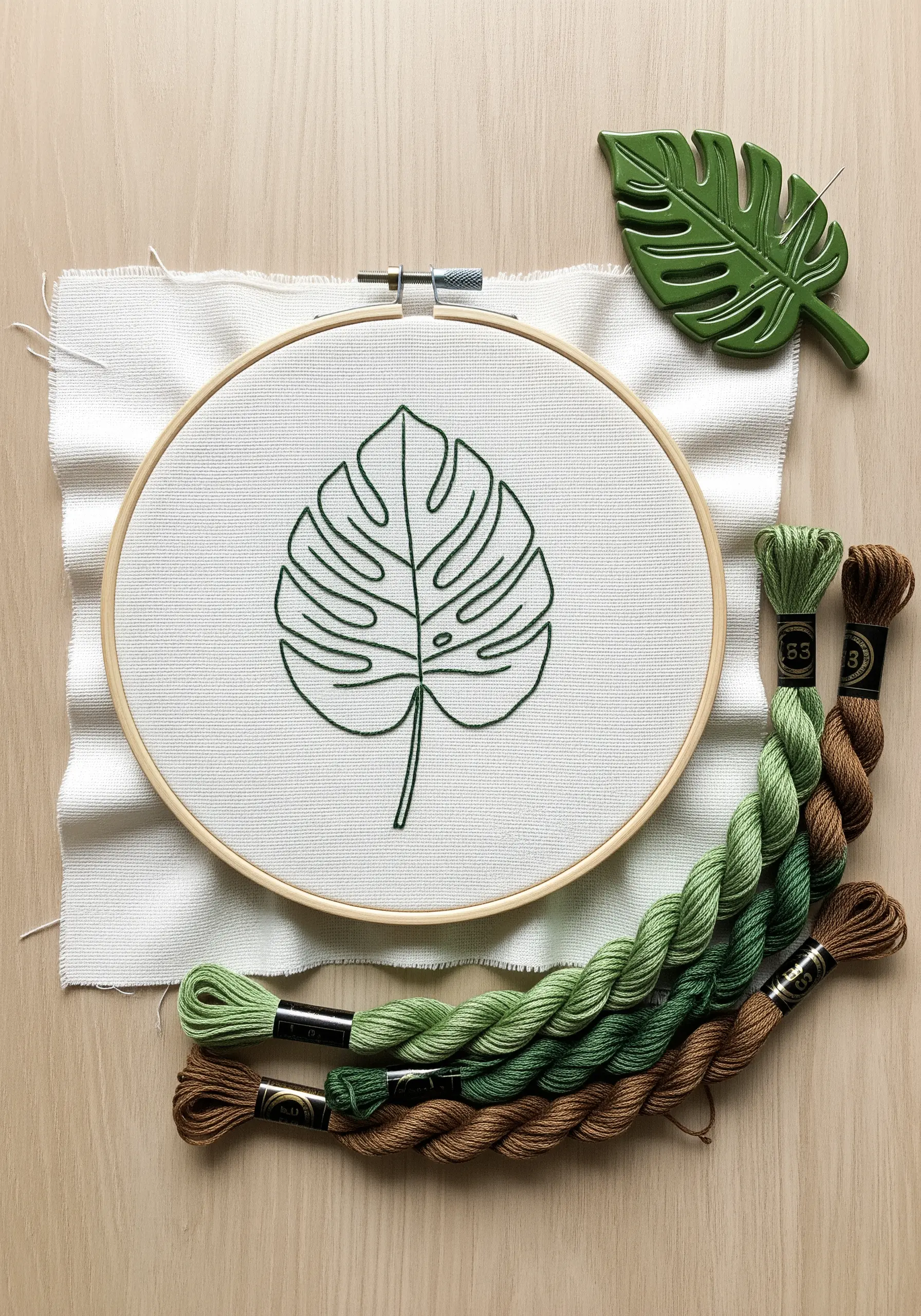 Green outline embroidery of a Monstera leaf on white fabric.