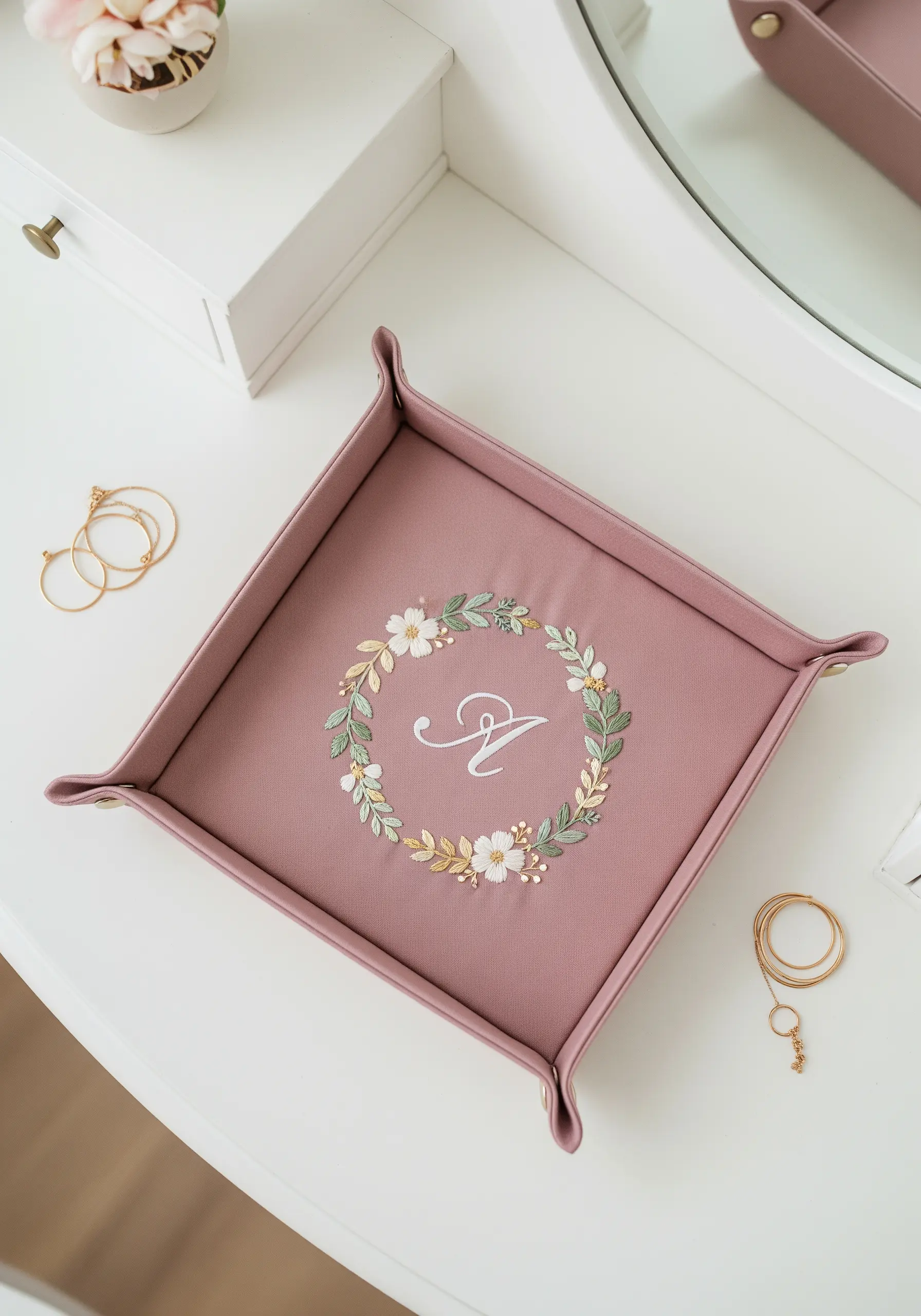 A dusty rose valet tray with a floral wreath and the initial 'A' embroidered in the center.