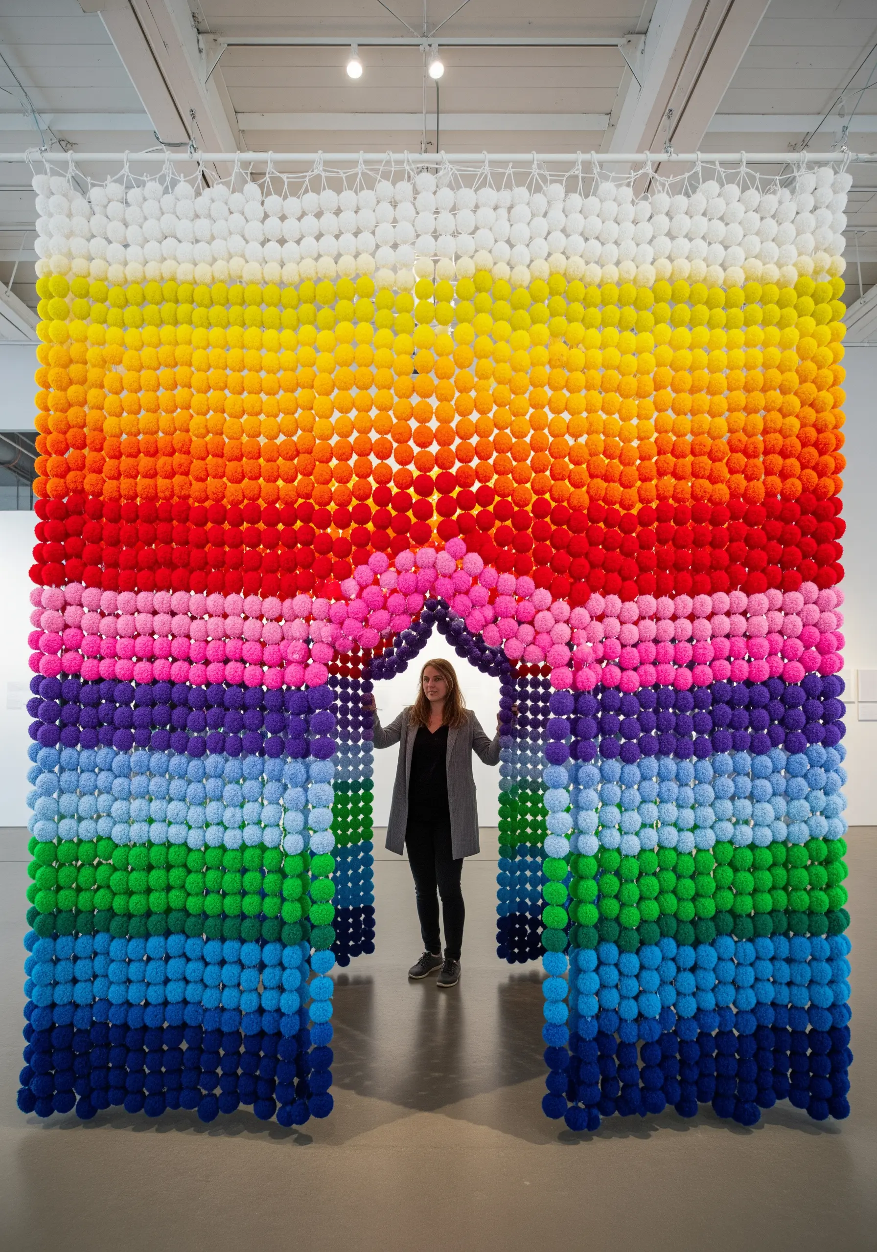 A large, arched installation made of hundreds of rainbow-colored pom-poms.