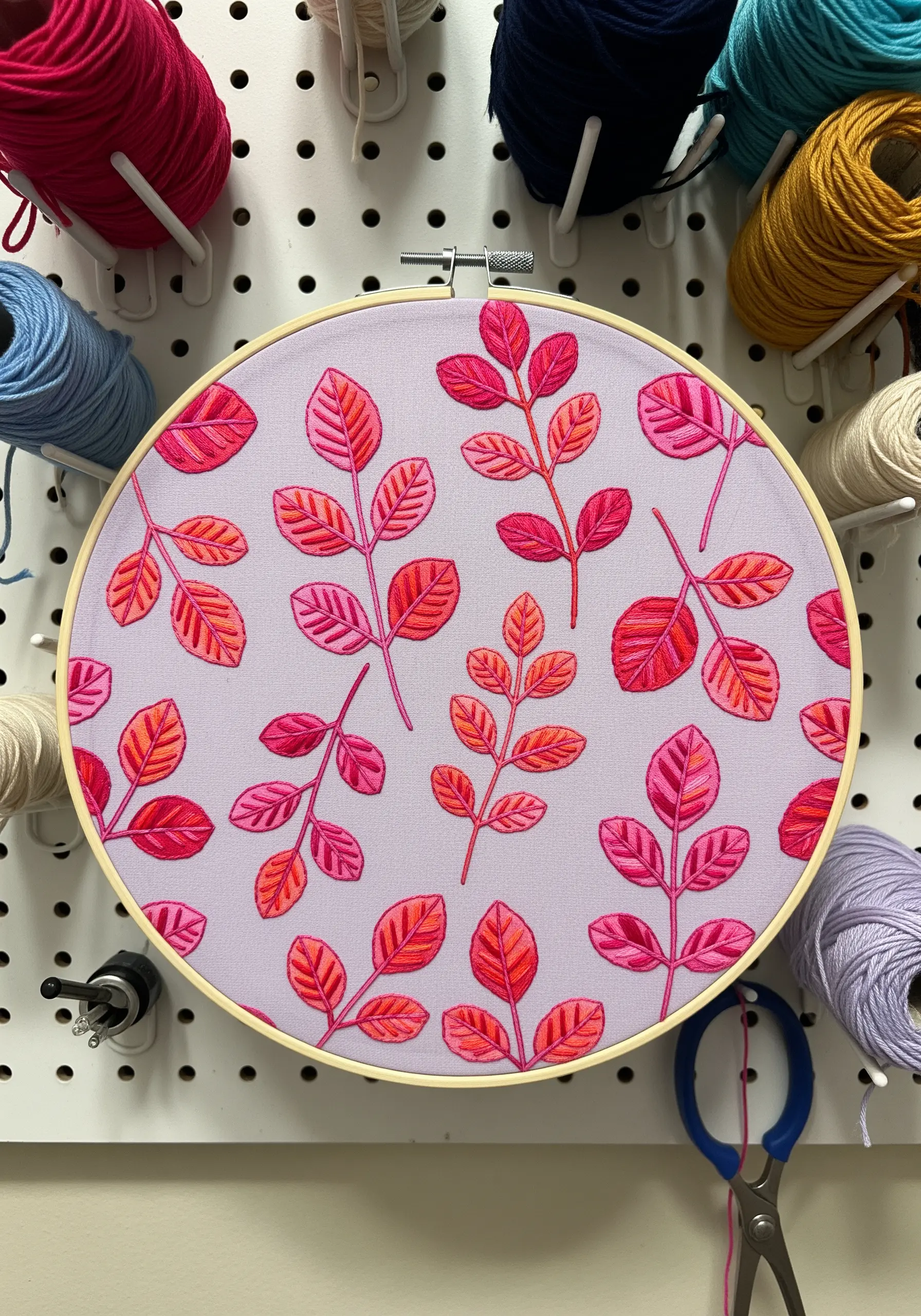 A repeating pattern of stylized leaves in vibrant pinks and oranges on a lavender fabric background.