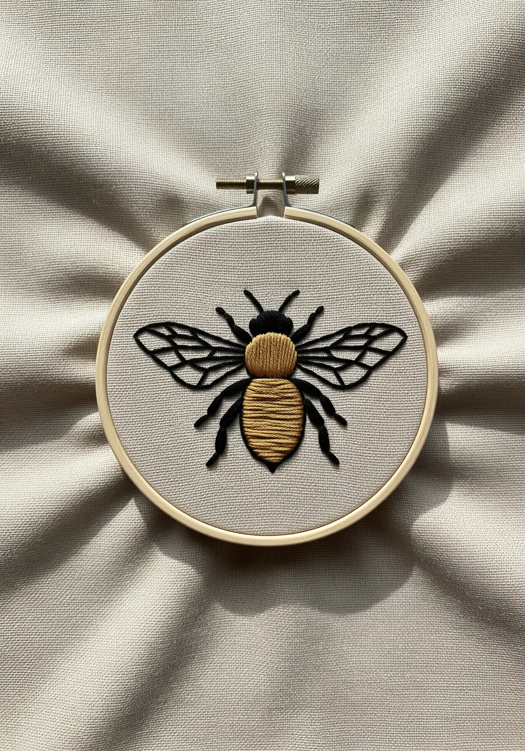 Embroidered bee with satin stitch body and backstitch wings in a hoop.